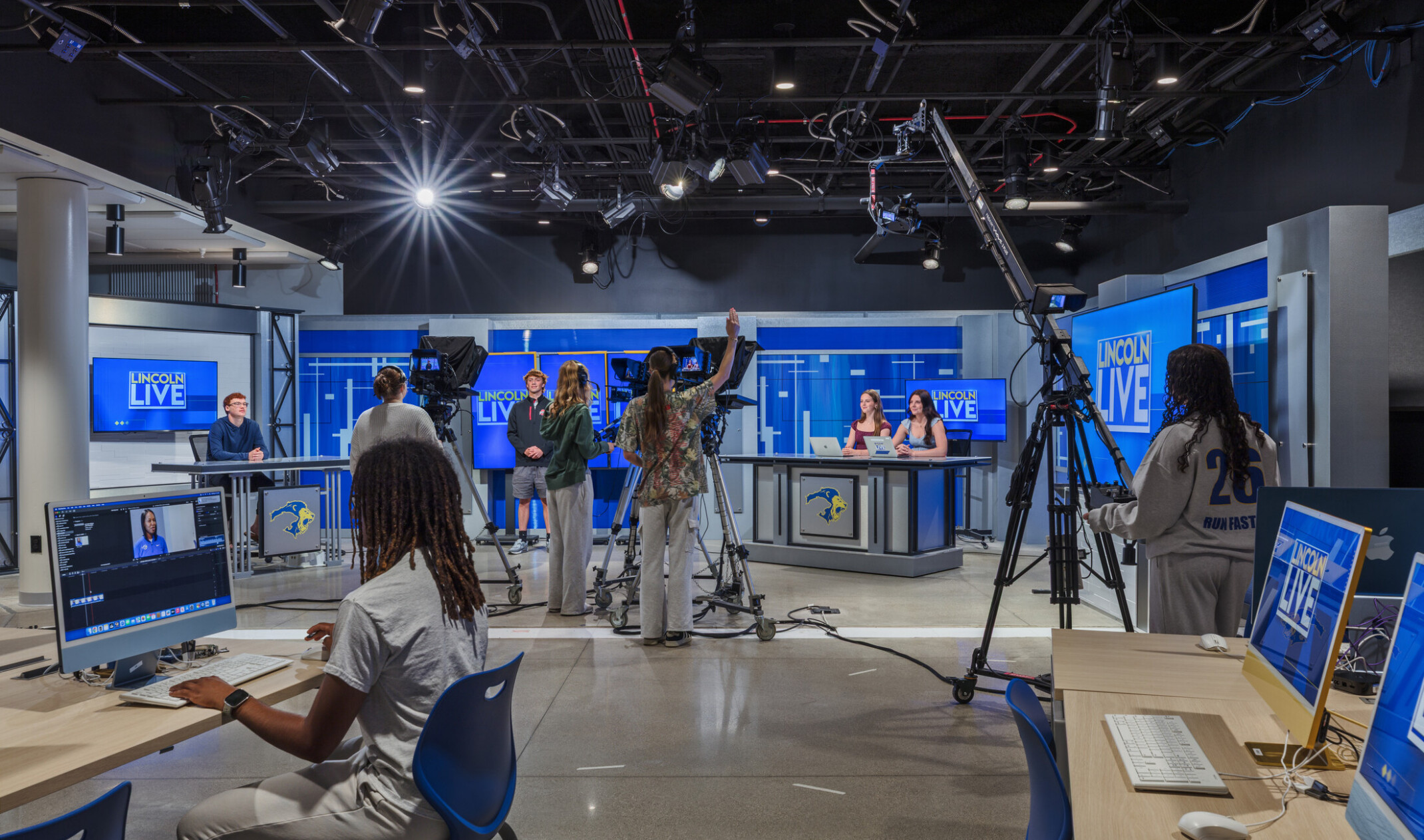 Student TV studio space; students at monitors and at news-desk style production set