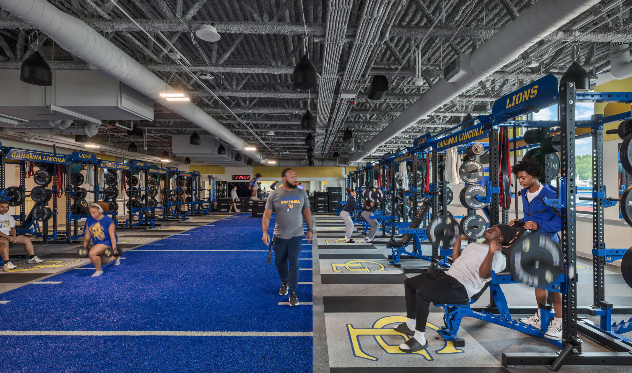 highschool weight room; blue and yellow branding with large weight machines lining each wall