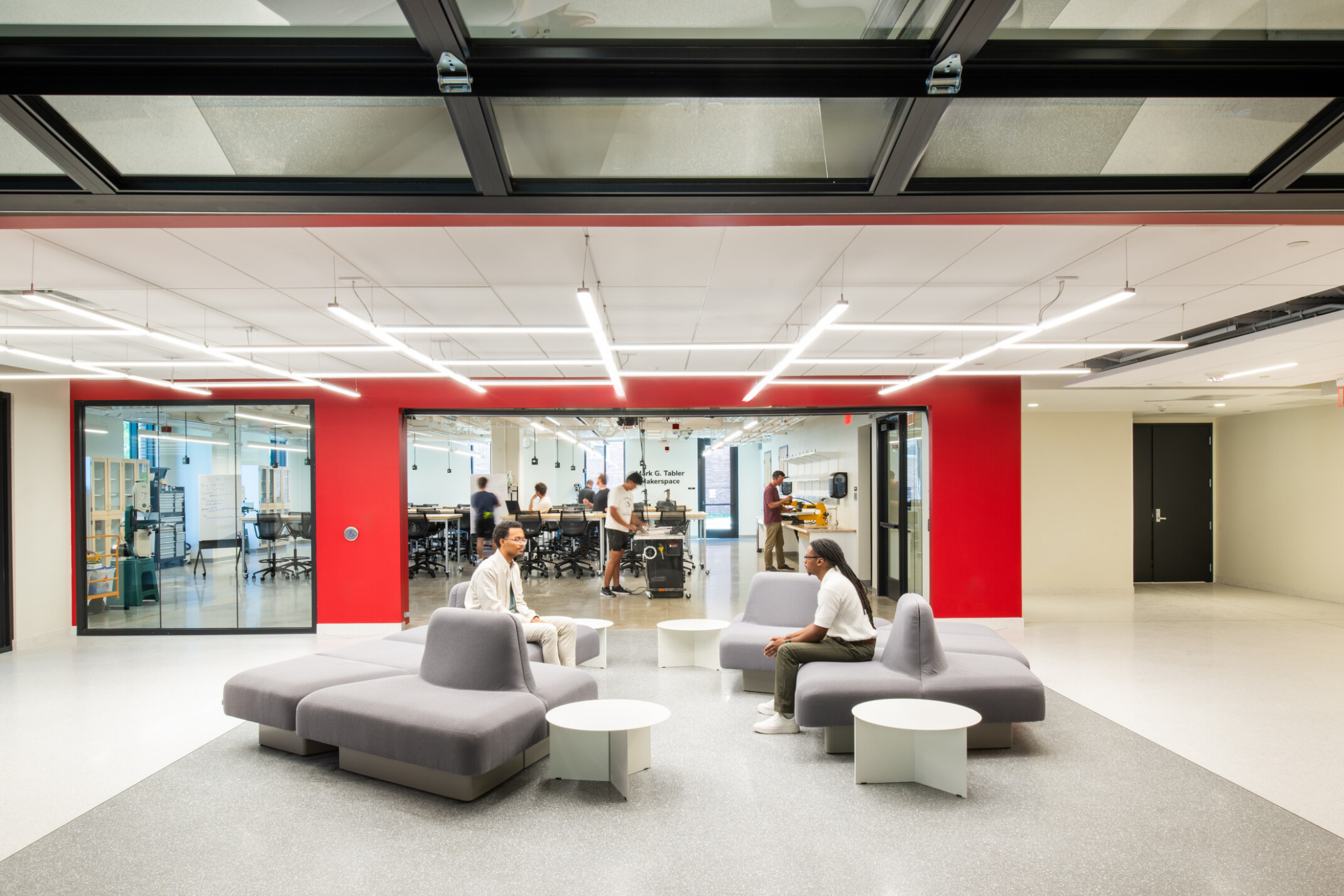 modern community space in a science building; comfortable modular, sitting space looks into an open concept lab behind floor to ceiling glass