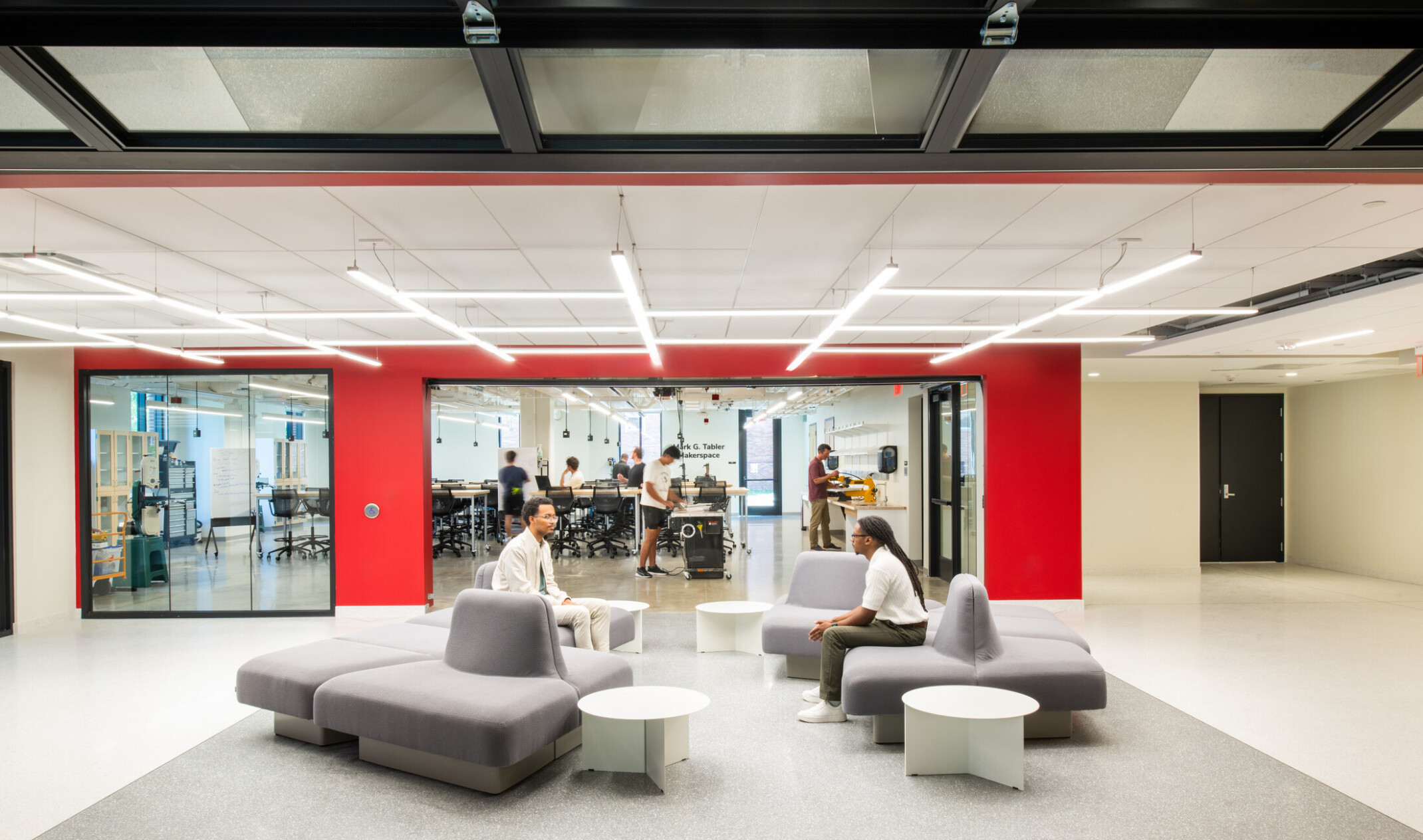modern community space in a science building; comfortable modular, sitting space looks into an open concept lab behind floor to ceiling glass