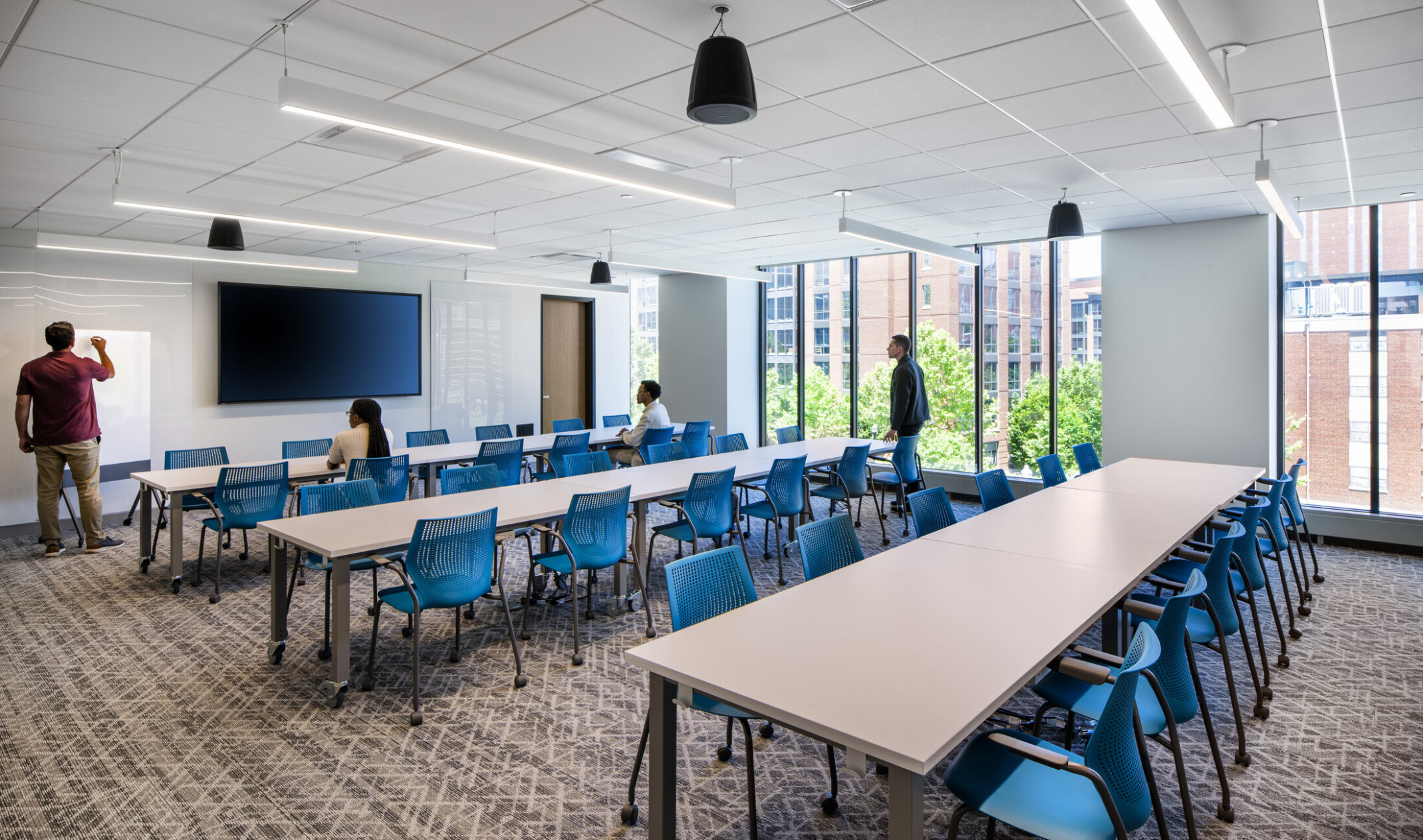 modern, naturally lit classroom with rows of tables facing a large TV and lecture stand