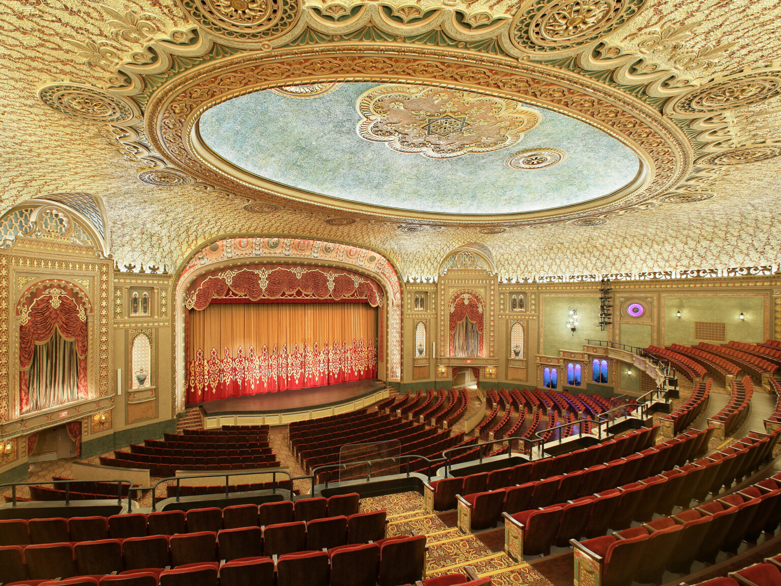 Interior of the Tennessee Theater, seen from the balcony looking to stage, ornate golden-patterned ceiling with round, recessed detail, dark red theatre seating