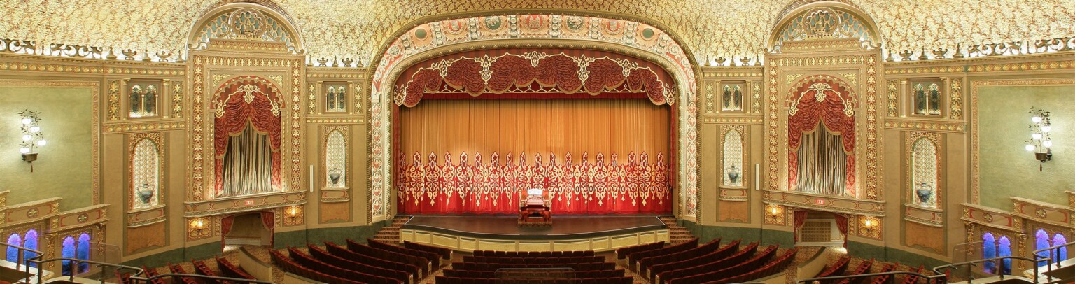 Audience gallery, from balcony looking to stage. Ornate patterned ceiling with round recessed detail illuminated at inner edge