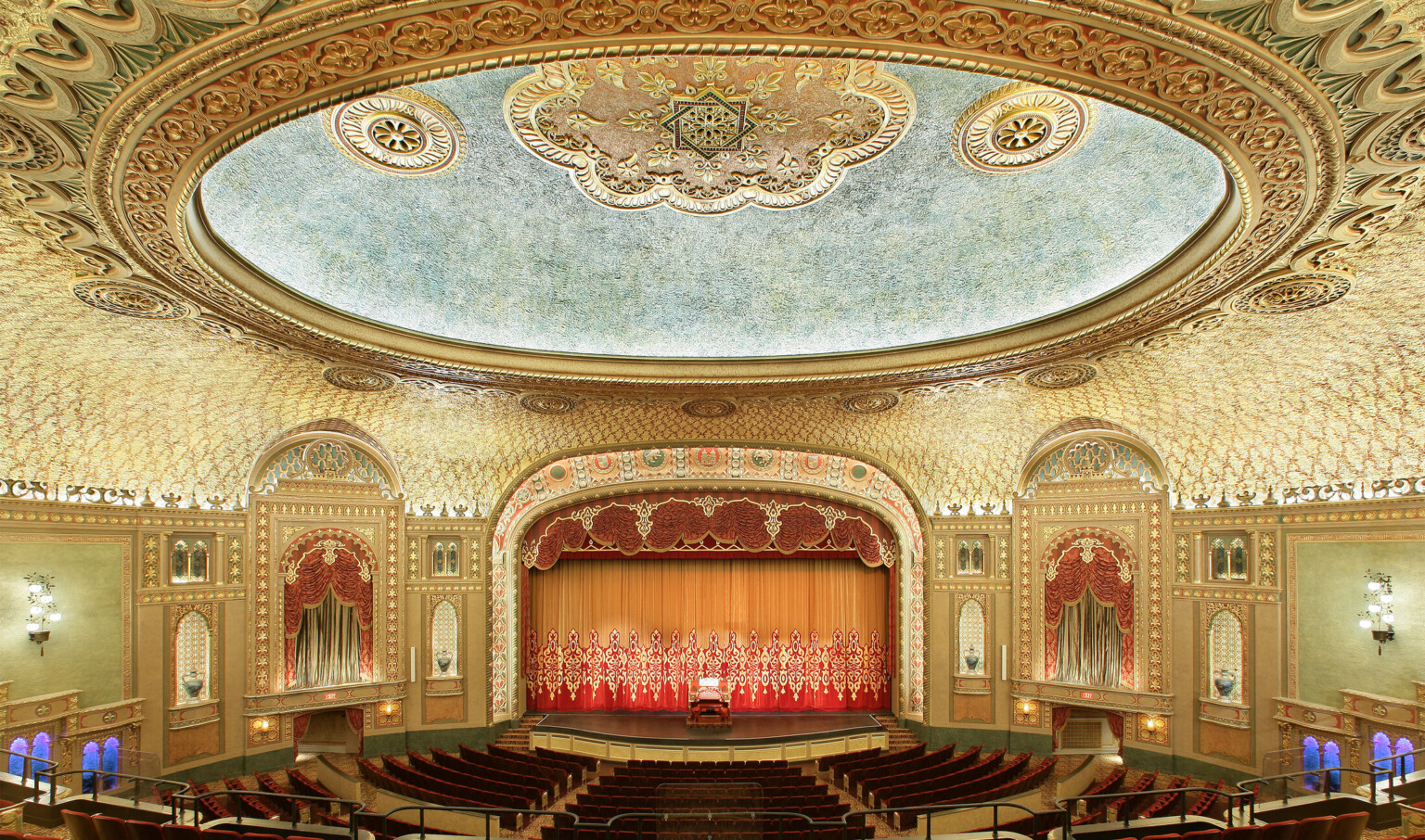 Audience gallery, from balcony looking to stage. Ornate patterned ceiling with round recessed detail illuminated at inner edge