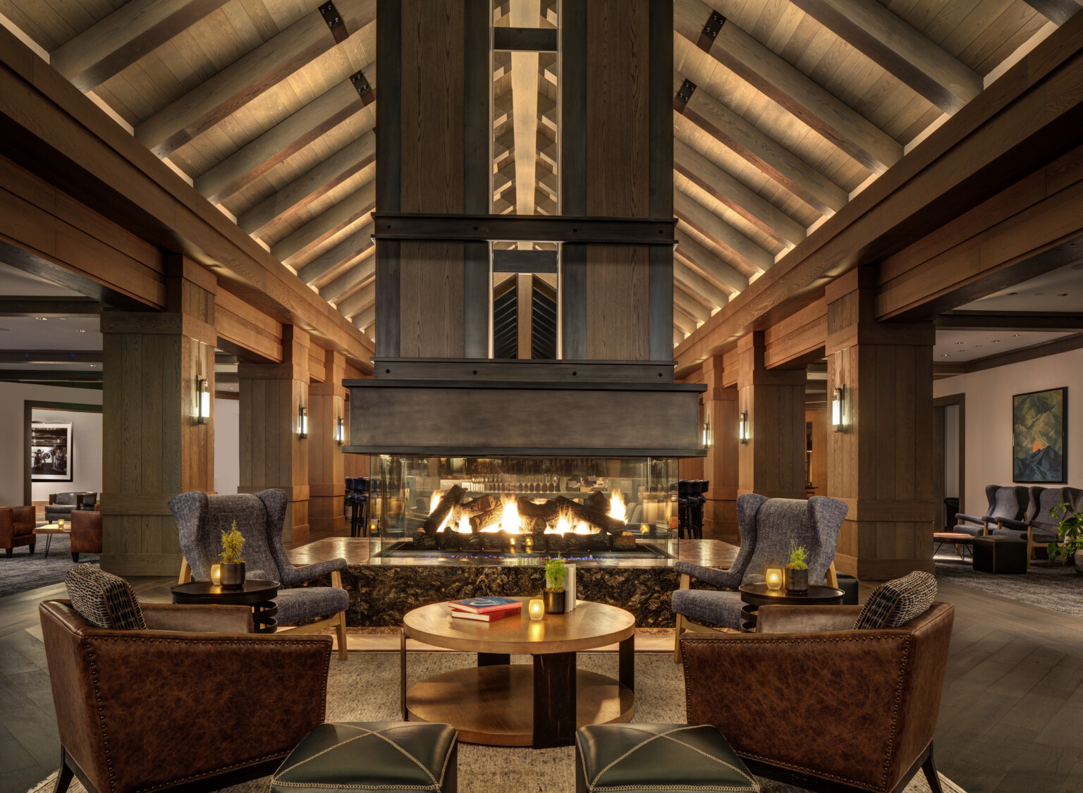 Cozy hotel lounge with a large double-sided fireplace, wooden ceiling beams and columns, and elegant seating arrangements throughout; dlr group design Cozy hotel lounge with a large double-sided fireplace, wooden ceiling beams and columns, and elegant seating arrangements throughout; dlr group design