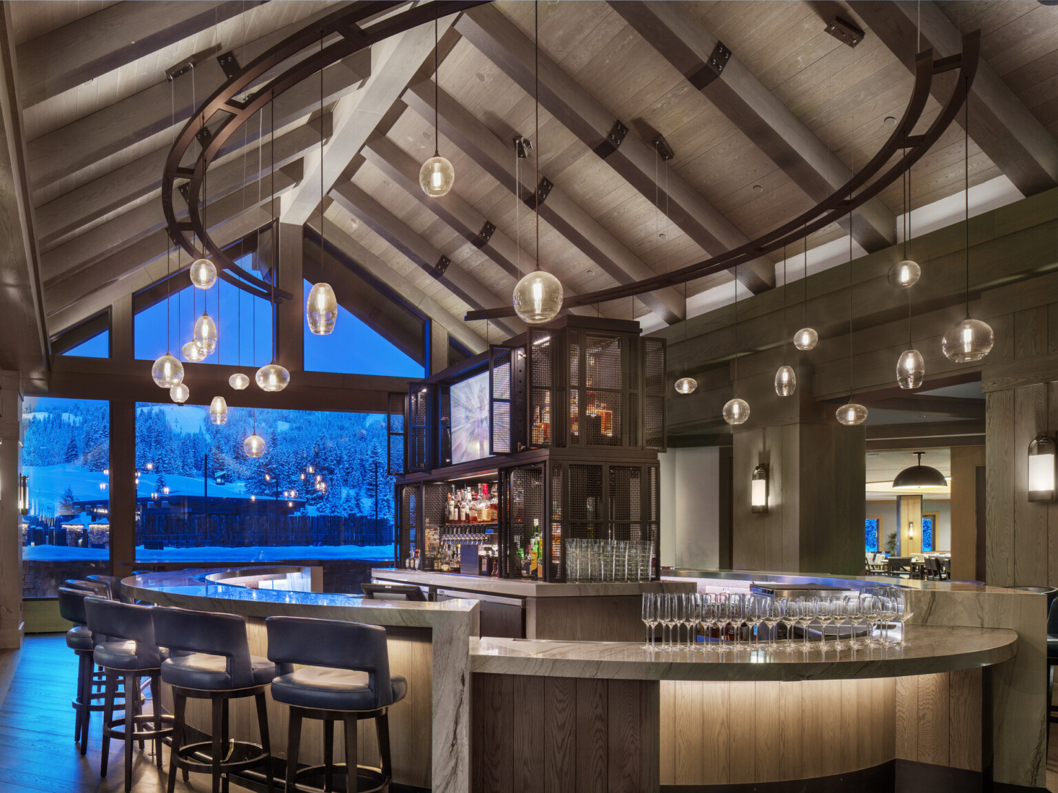 An elegant hotel bar with pendant lights and a view of a snowy landscape through large windows