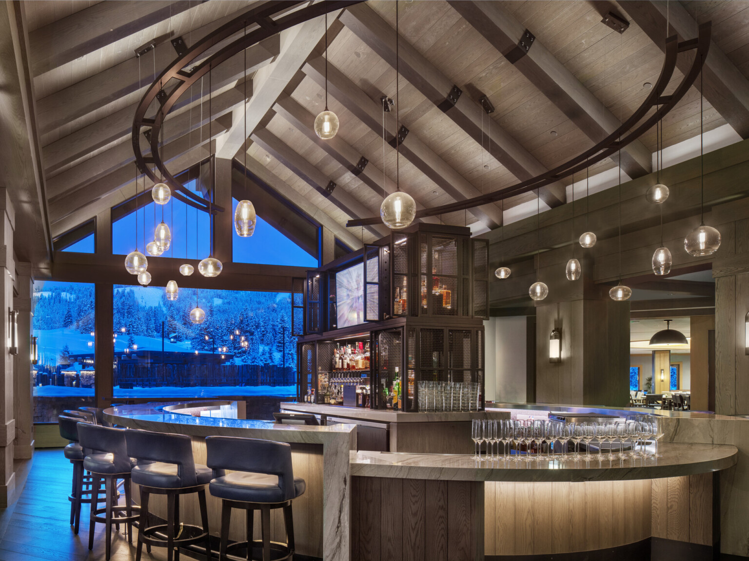 An elegant hotel bar with pendant lights and a view of a snowy landscape through large windows