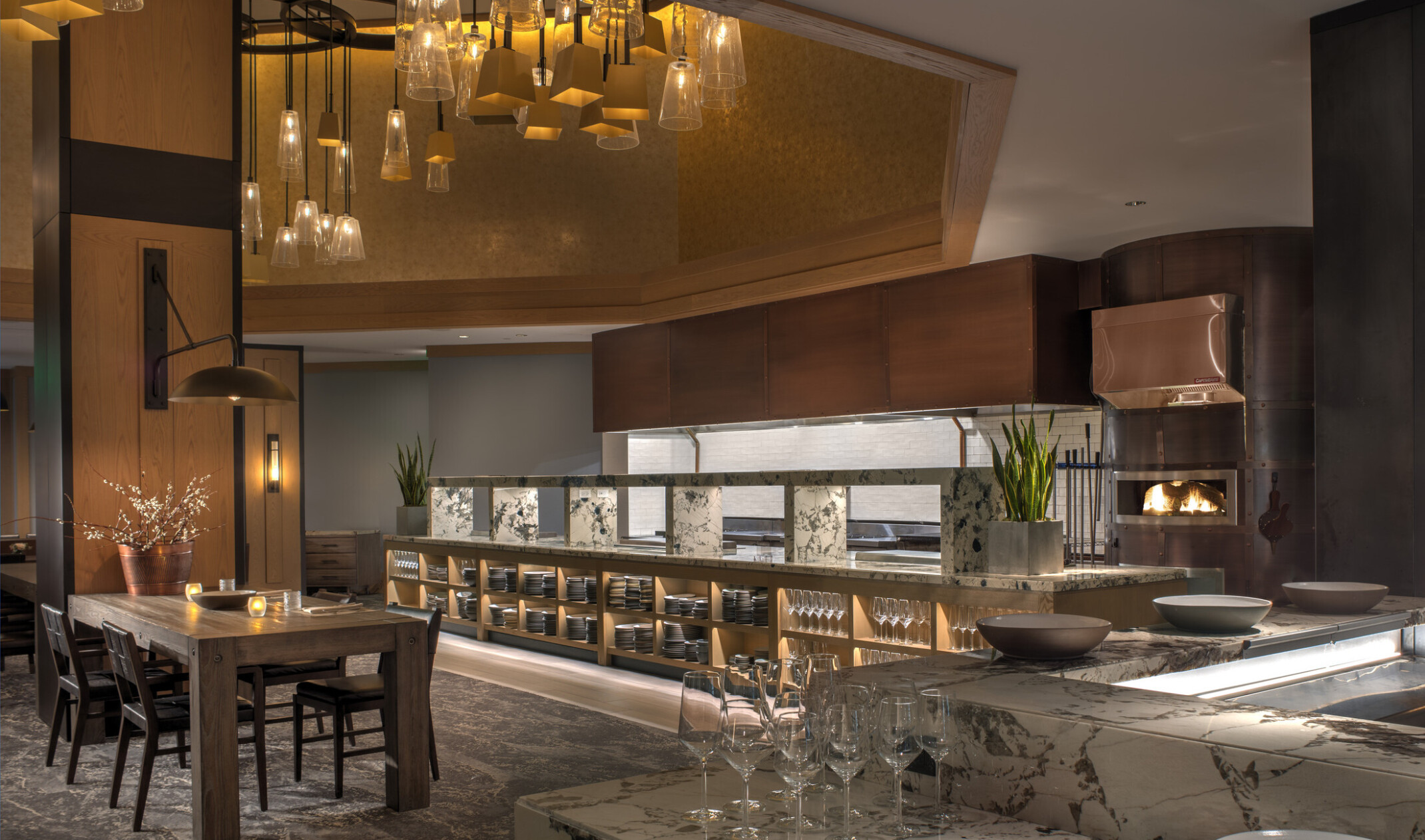 Modern hotel restaurant interior with a dining table, marble countertop, and open kitchen.
