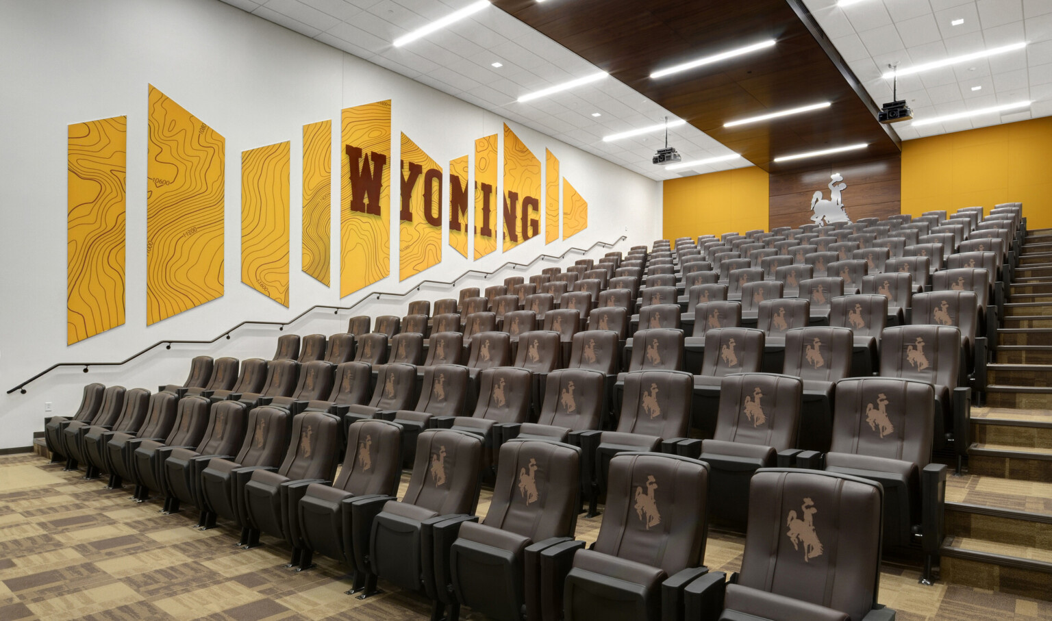 Brown theater style stadium seats with logos in white room with yellow mural reading Wyoming on left wall. Yellow back wall