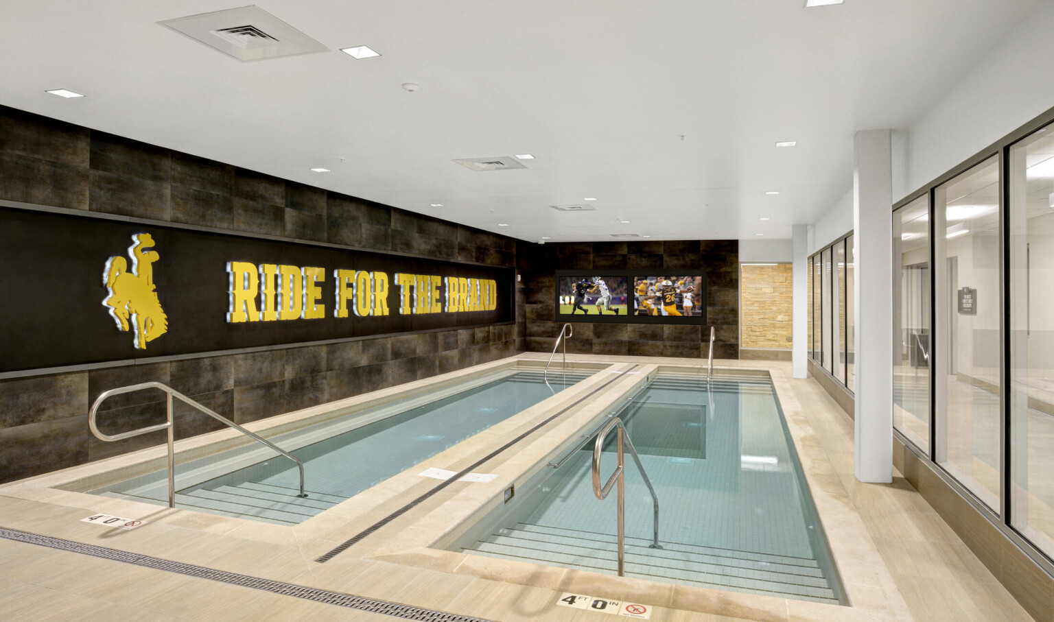 2 recovery pools in stone room with glass wall, right. Backlight logo, left, with Ride for the Brand phrase. Screens front