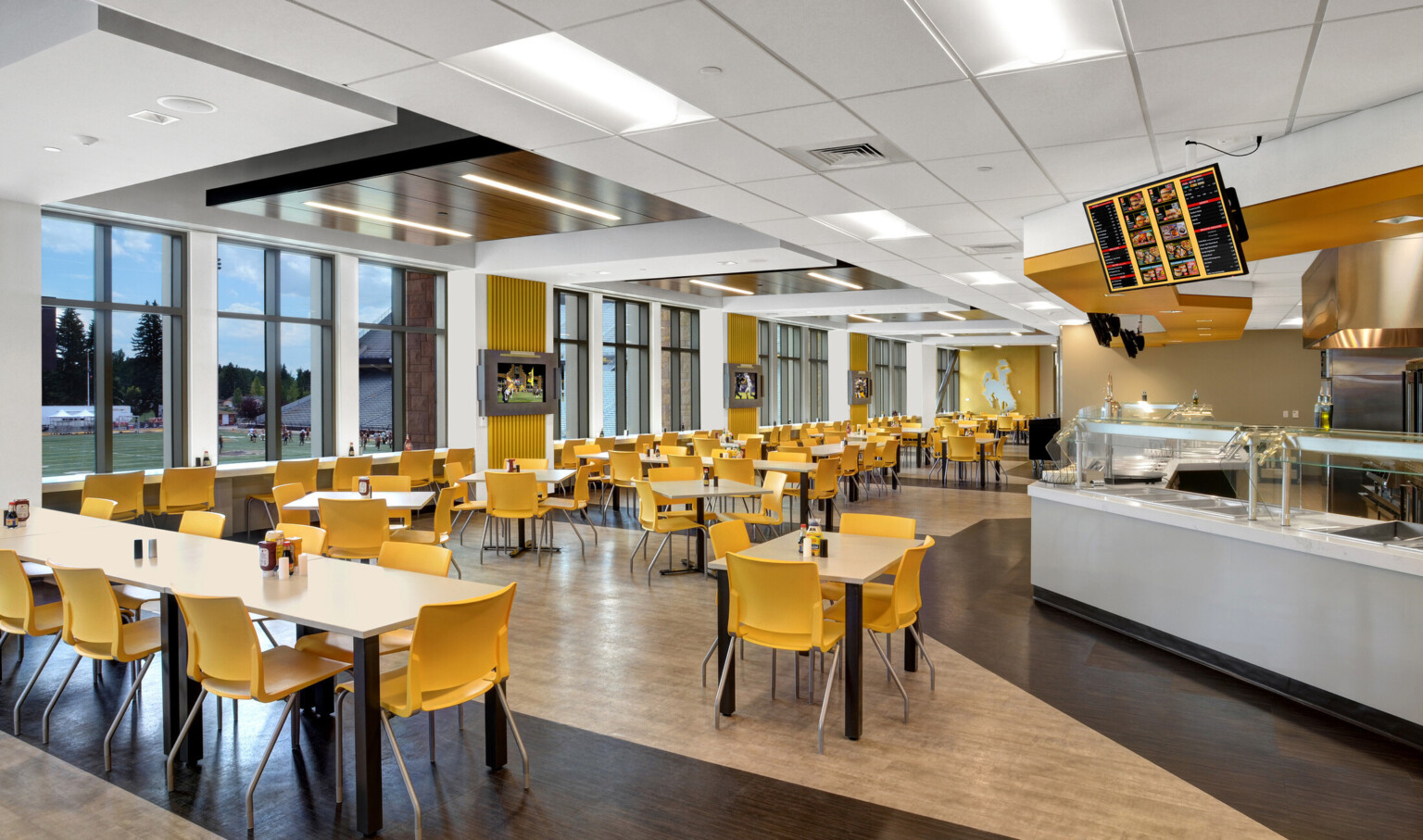 Nutrition Center dining space with tables by floor to ceiling windows, left, looking to field. Cafeteria counter right