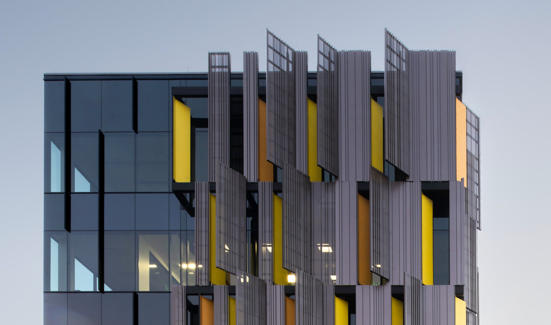 side view of courthouse with serrated sunscreen facade, a pattern of yellow panels peaking between. Floor to ceiling windows side view of courthouse with serrated sunscreen facade, a pattern of yellow panels peaking between. Floor to ceiling windows