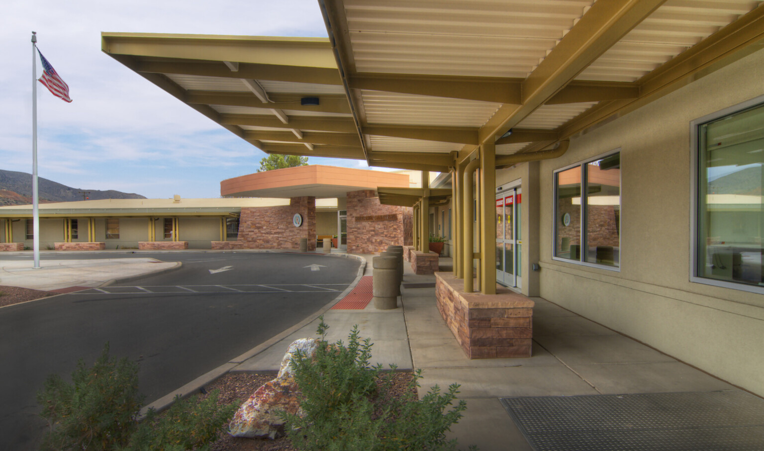 Rendering of front of building near emergency room entry. White textured overhang seen from beneath with yellow pillars