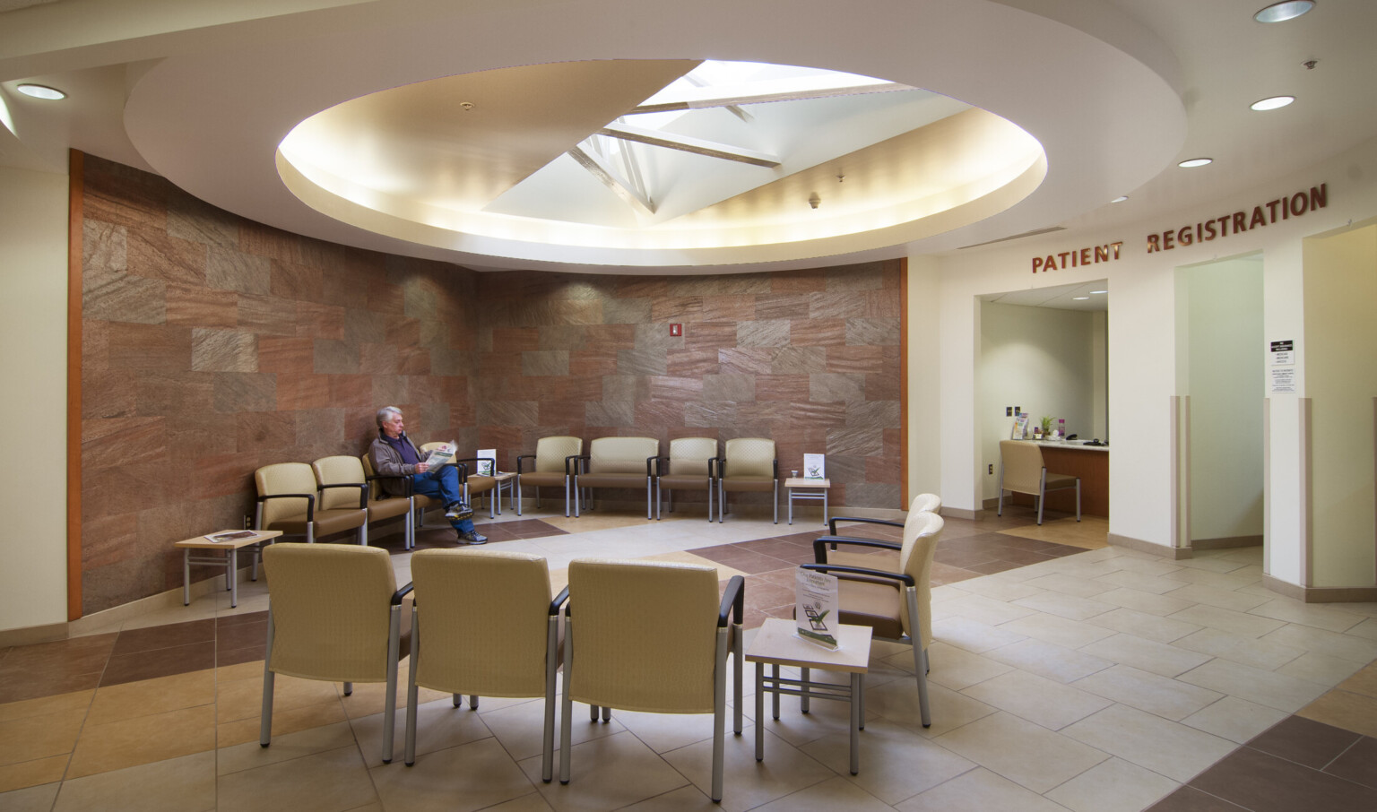 Reception in round room with tile wall and recessed geometric ceiling detail, white registration area and wood desk right