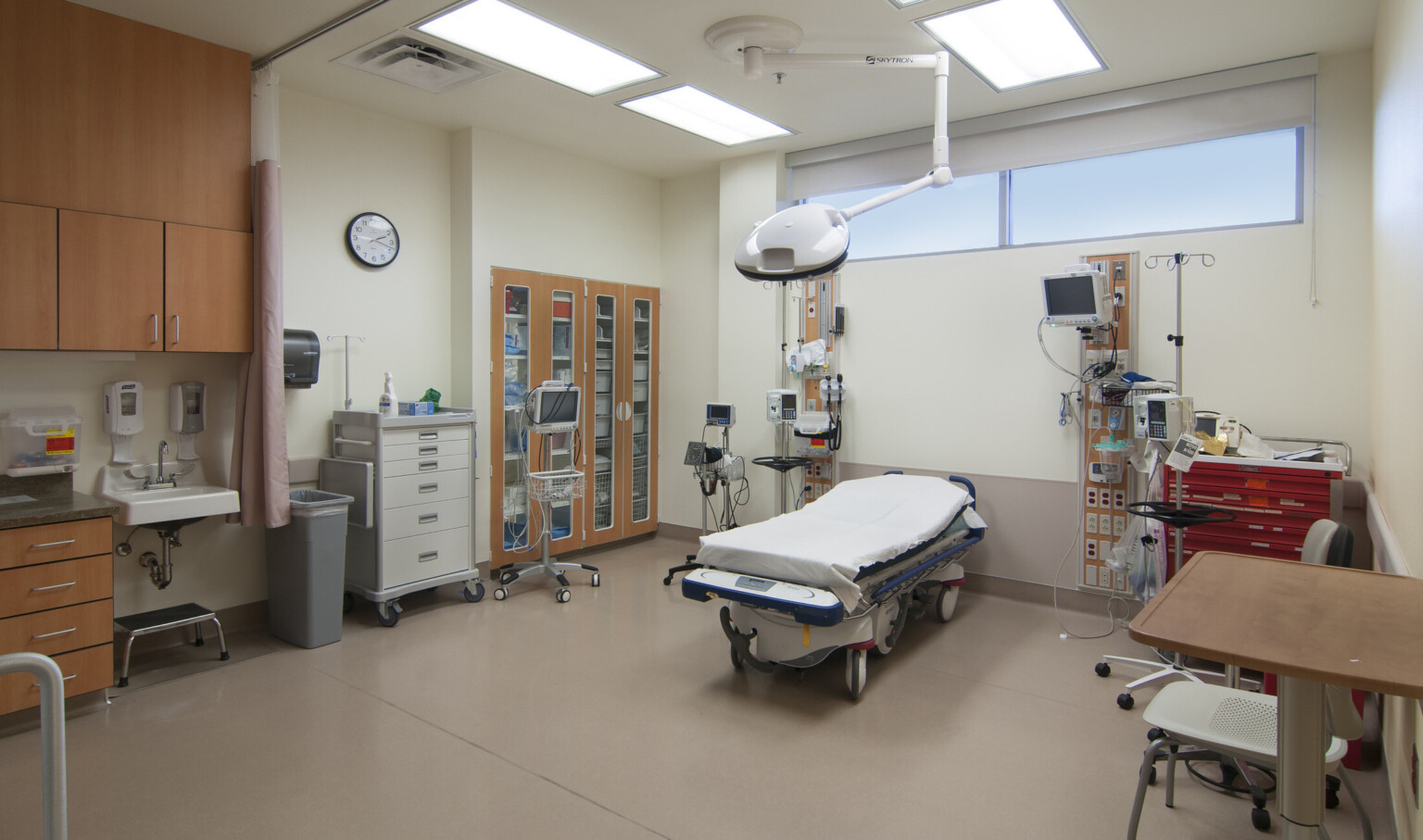 Hospital bed center equipment on wall on both sides. Built in cupboard with wood doors on left wall next to medical cart