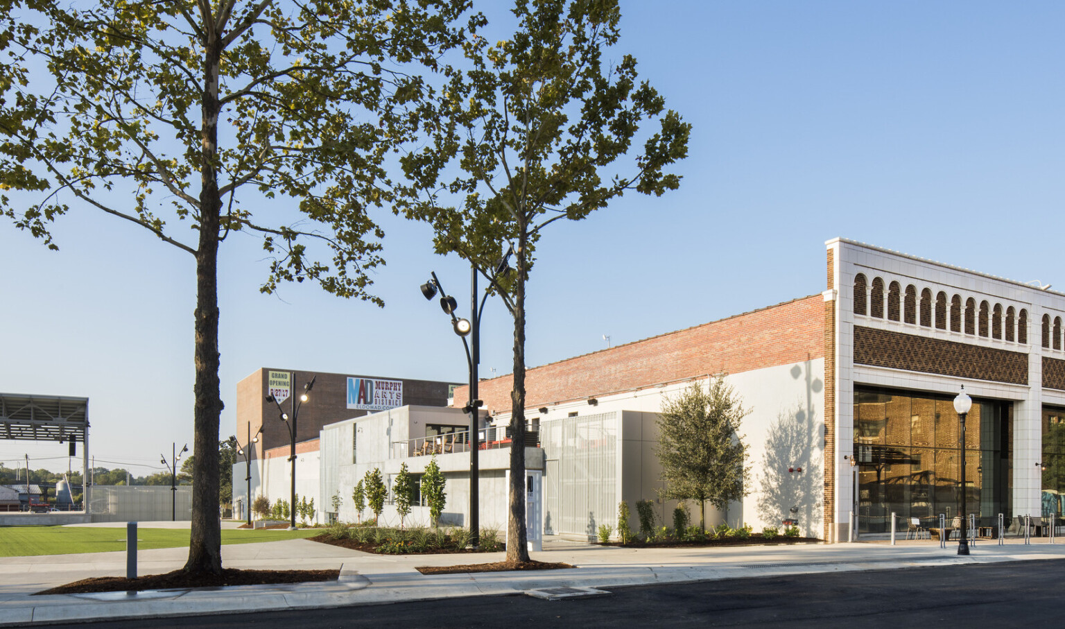Corner view of brick building with white molded facade next to green field with pavilion roof