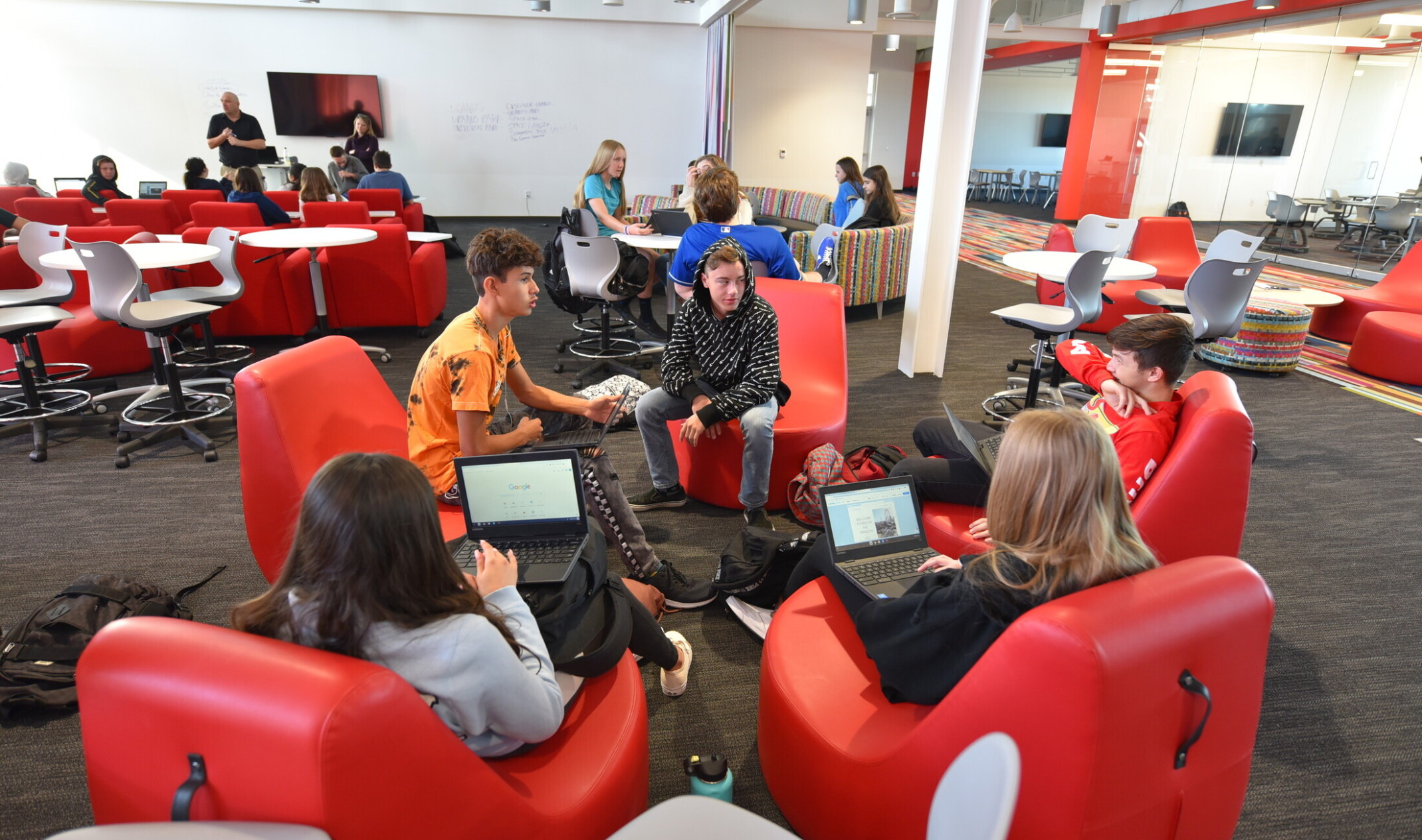 students sitting in a circle in ergonomic red chairs in flexible learning space off hallway with glass walls and red accents