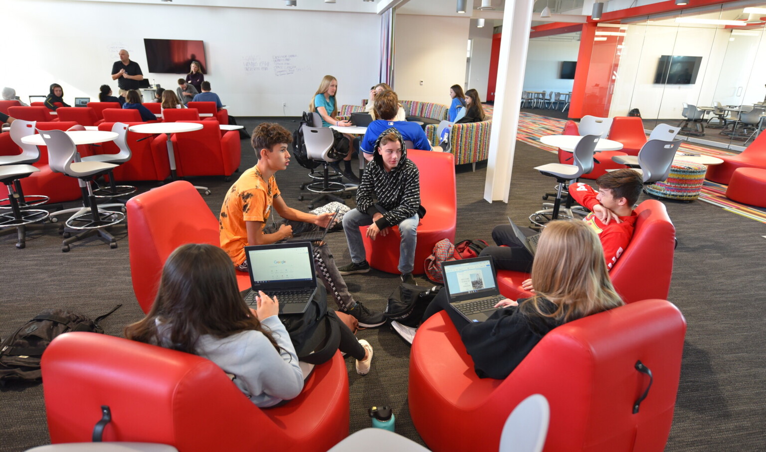 Students working on laptops in red ergonomic chairs in a large open learning space with flexible seating Students working on laptops in red ergonomic chairs in a large open learning space with flexible seating