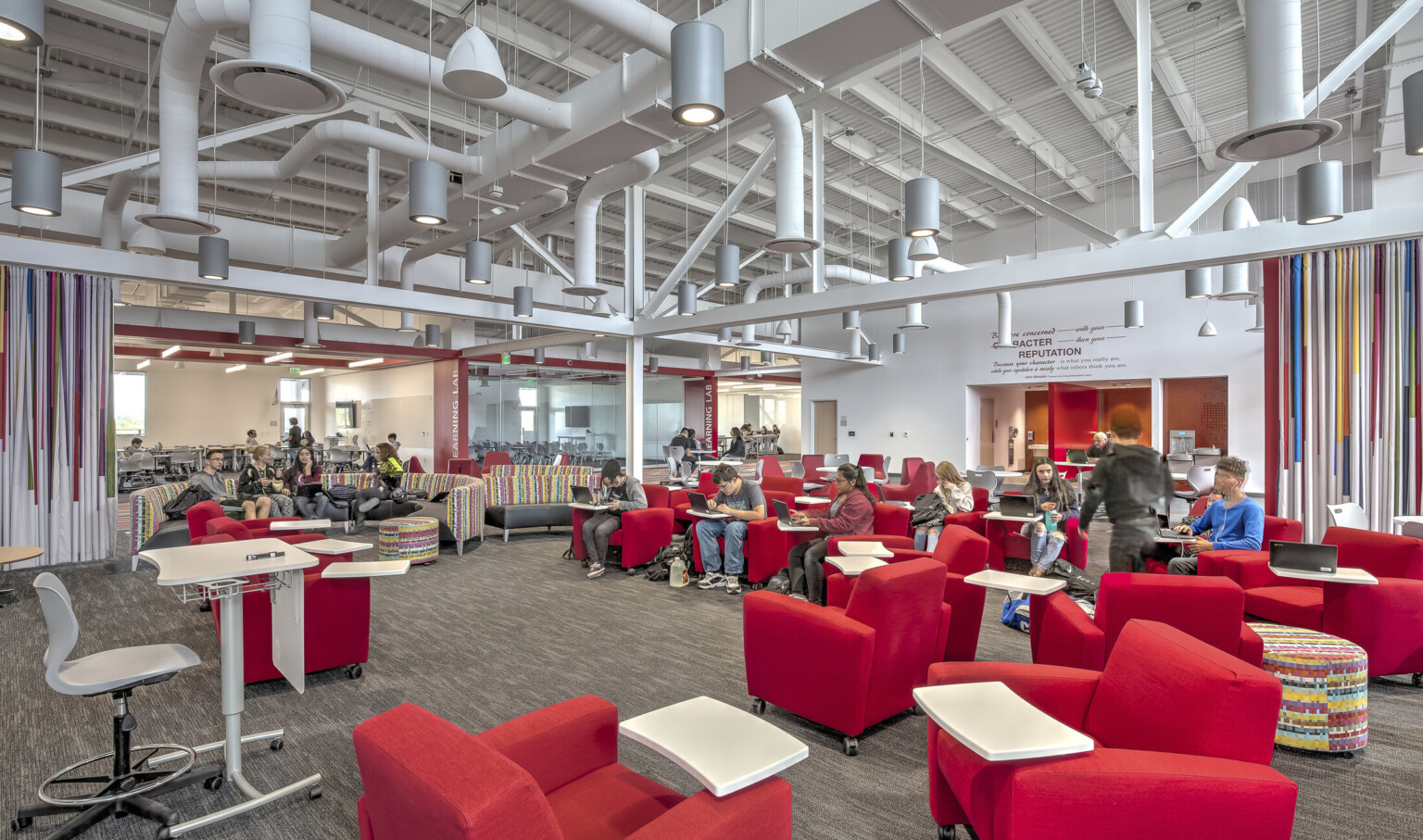 Large carpeted white room with red armchairs. Striped accent walls. Exposed ductwork and hanging pendant lights overhead Large carpeted white room with red armchairs. Striped accent walls. Exposed ductwork and hanging pendant lights overhead