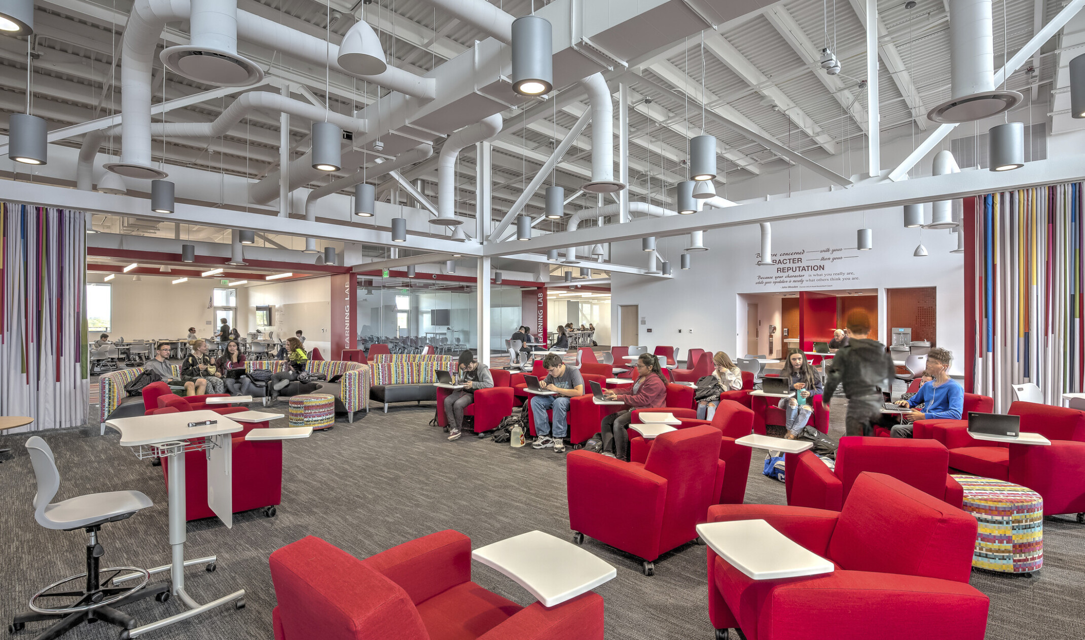 Large carpeted white room with red armchairs. Striped accent walls. Exposed ductwork and hanging pendant lights overhead