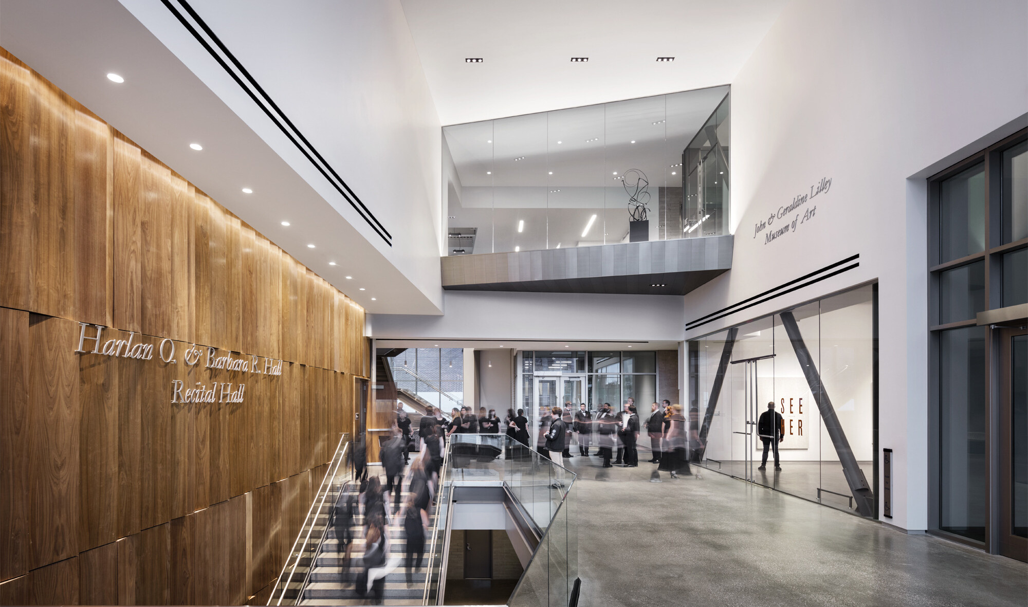 A staircase next to textural wood wall with view behind of 3rd story gallery glass balcony
