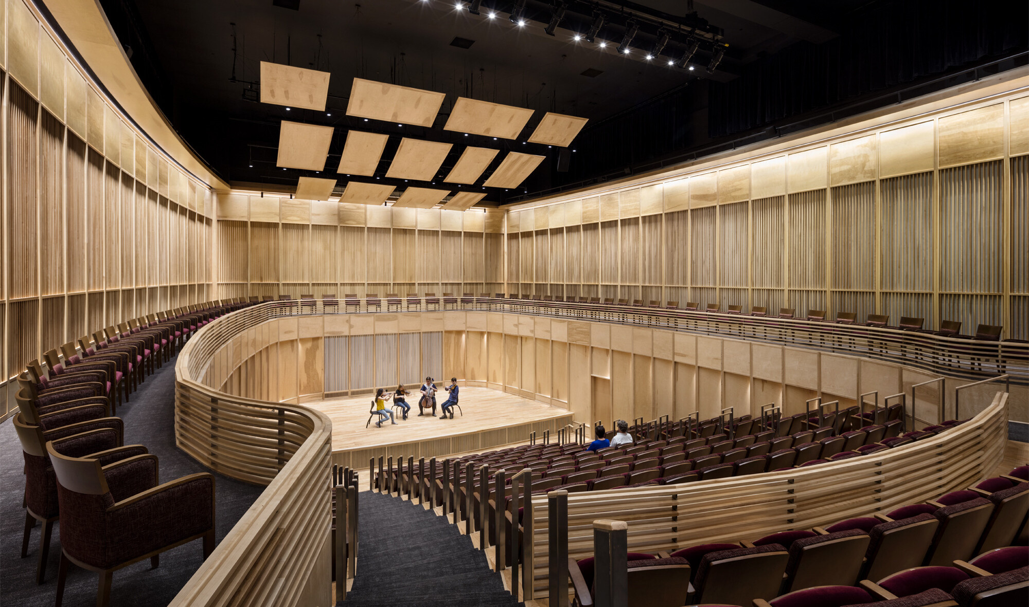 View from the back of wooden wall oval auditorium with 4 musicians on stage and 2 people seated in the audience