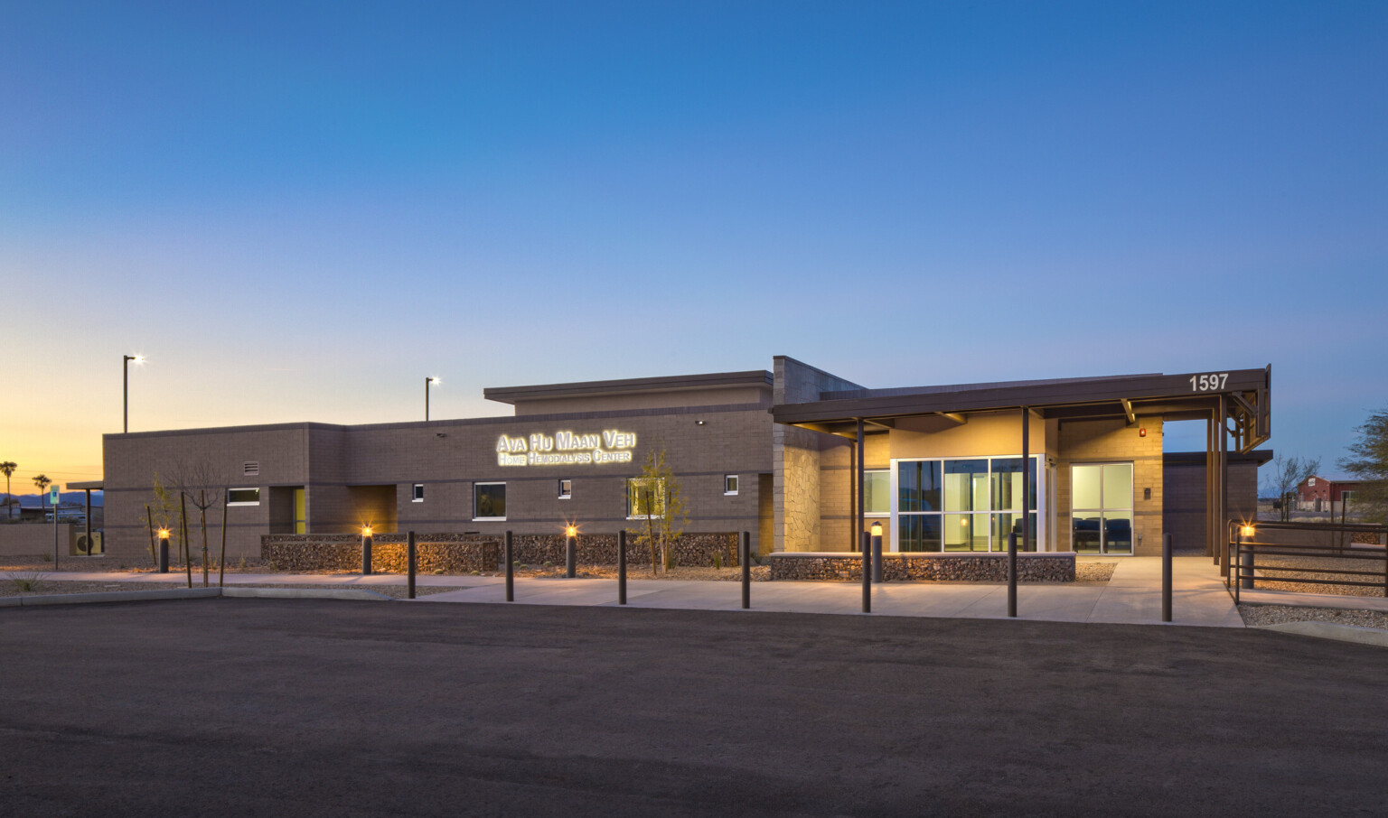 Front of building illuminated from recessed lights in overhang. Lit sign left reads Ava Hu Maan Veh Home Hemodialysis Center