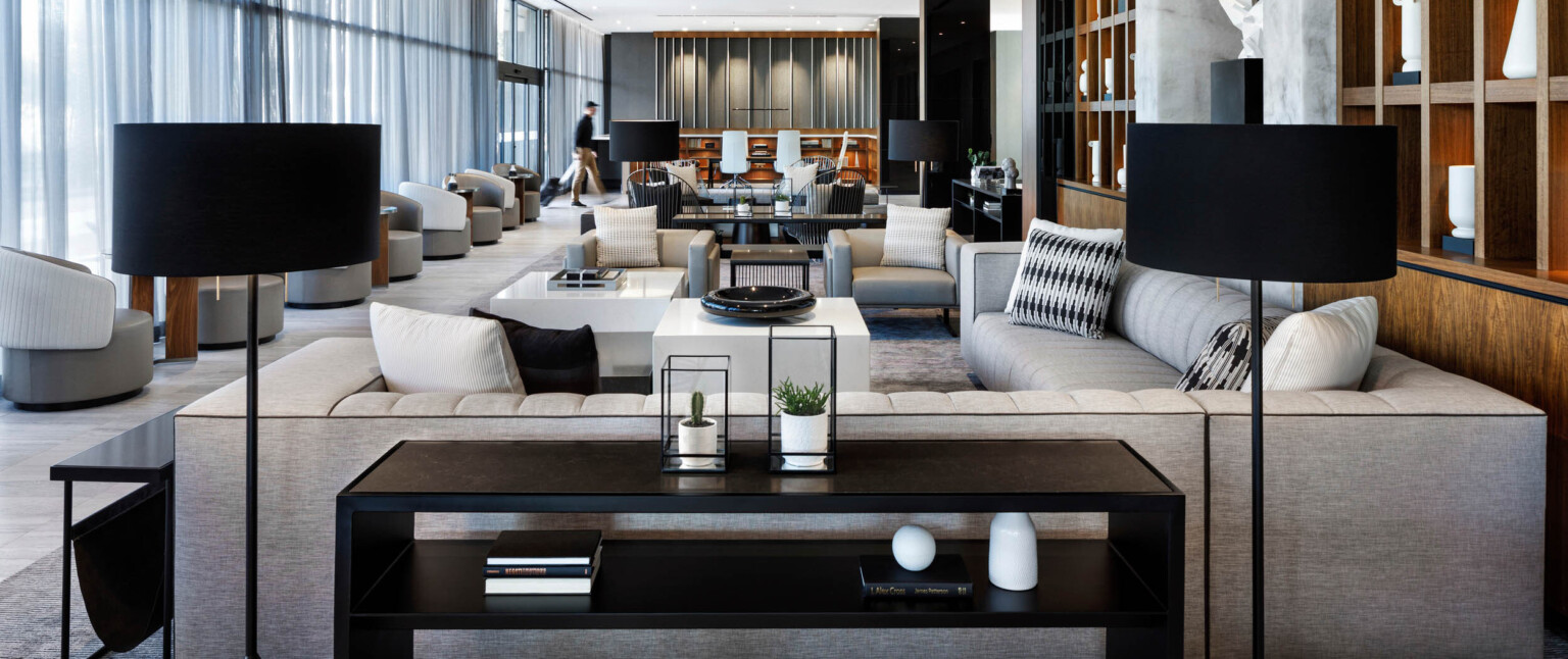 Mixed seating area in lobby with tables. Square wooden shelves to the right of the area, and floor to ceiling windows on left following Marriott brand architecture