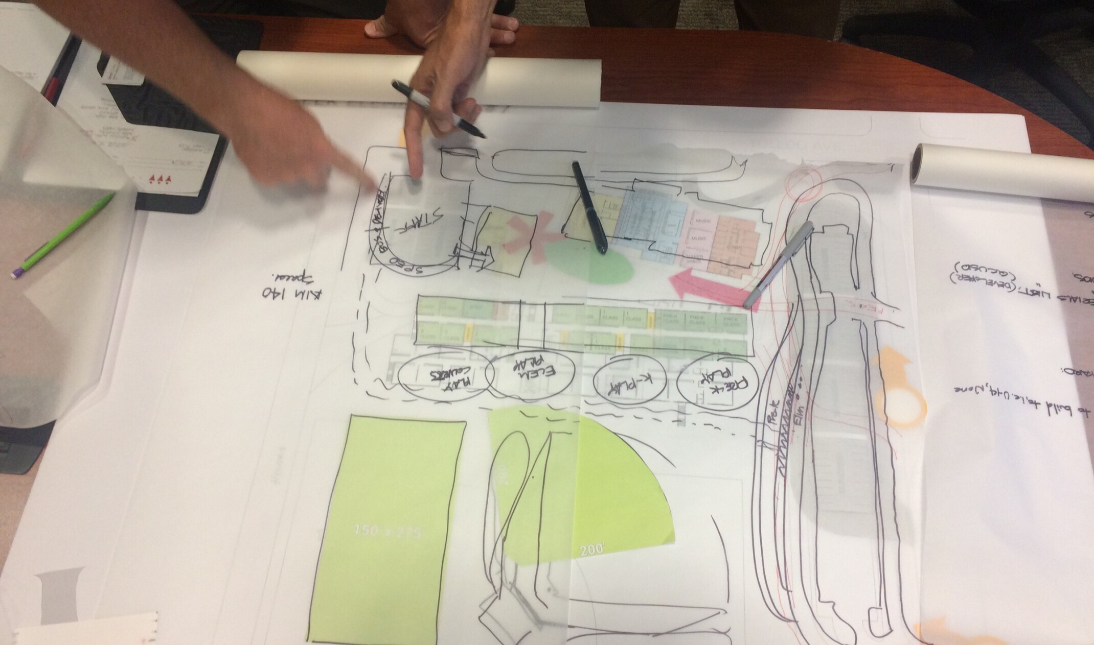 2 people working on a hand drawn rendering, each pointing to the same point in the top left of the photo