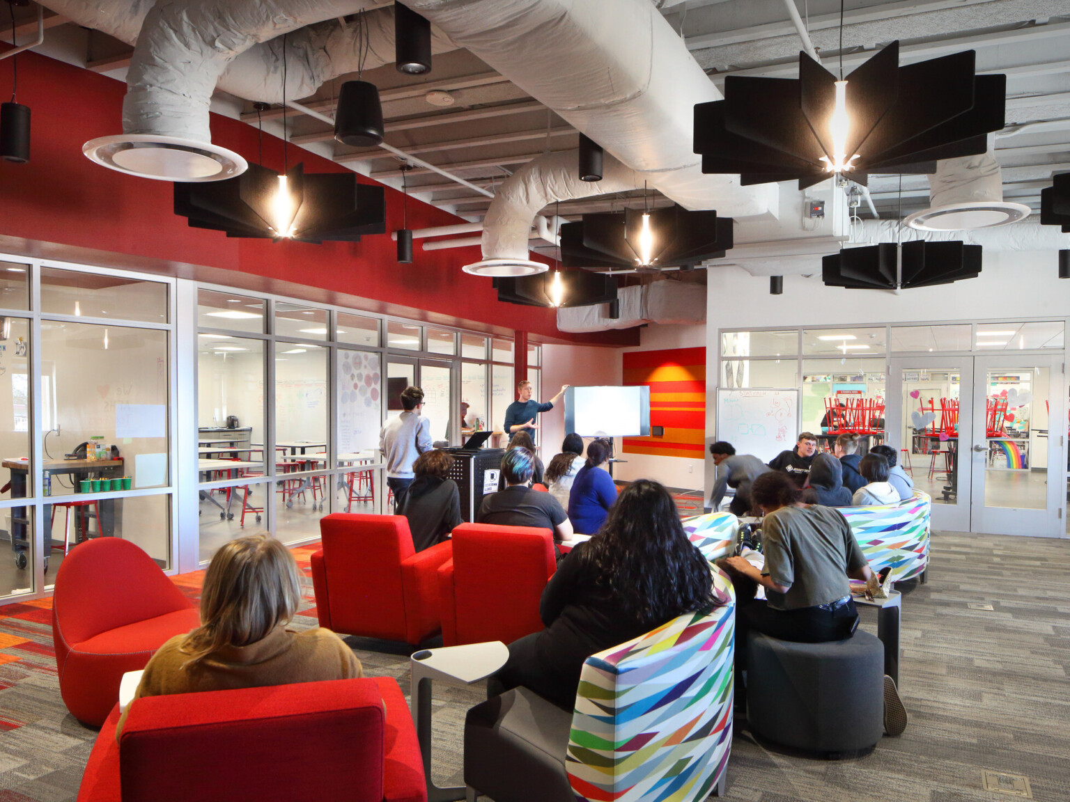 classroom red accent wall, red upholstered seating, bright white exposed ductwork, glass divider wall