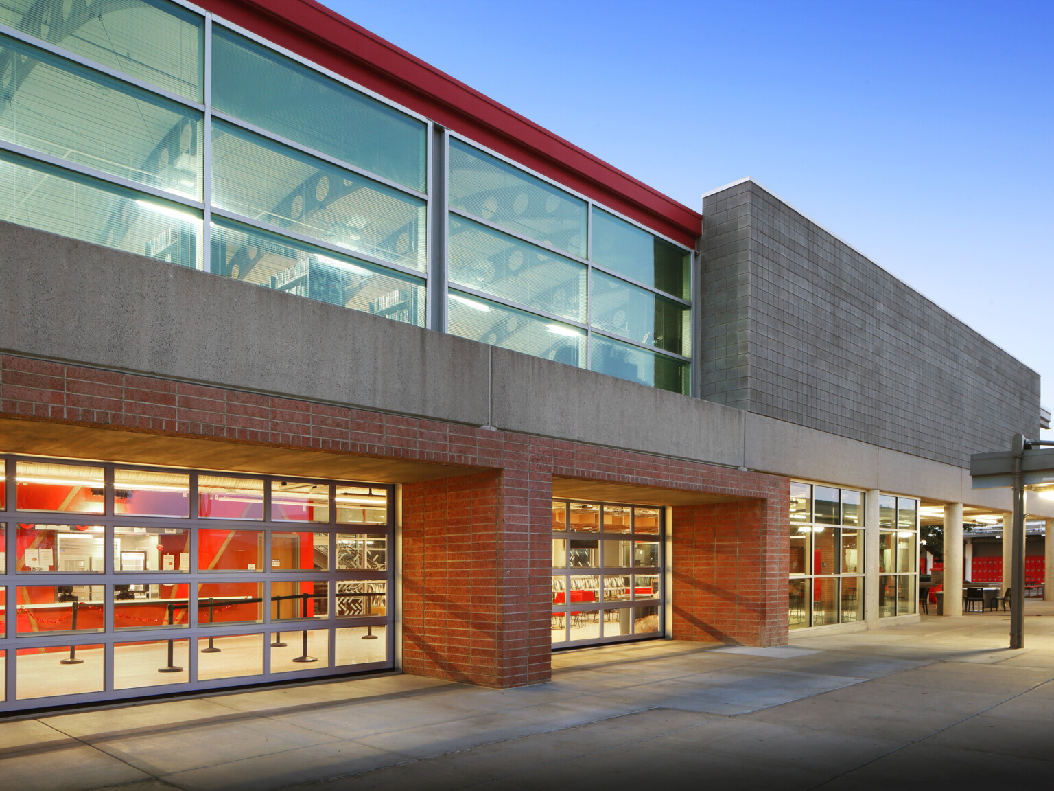 Exterior view of red and grey brick facade, steel, floor-to-ceiling window panels, concrete walkway