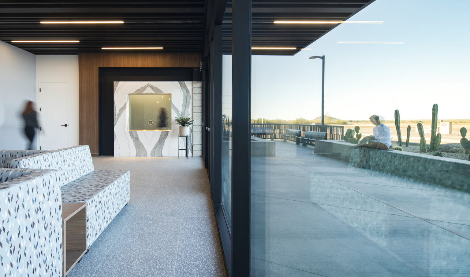 a lobby with bookmatched stone feature wall, stone tile floor and black slatted ceiling with a glass wall overlooking cactus