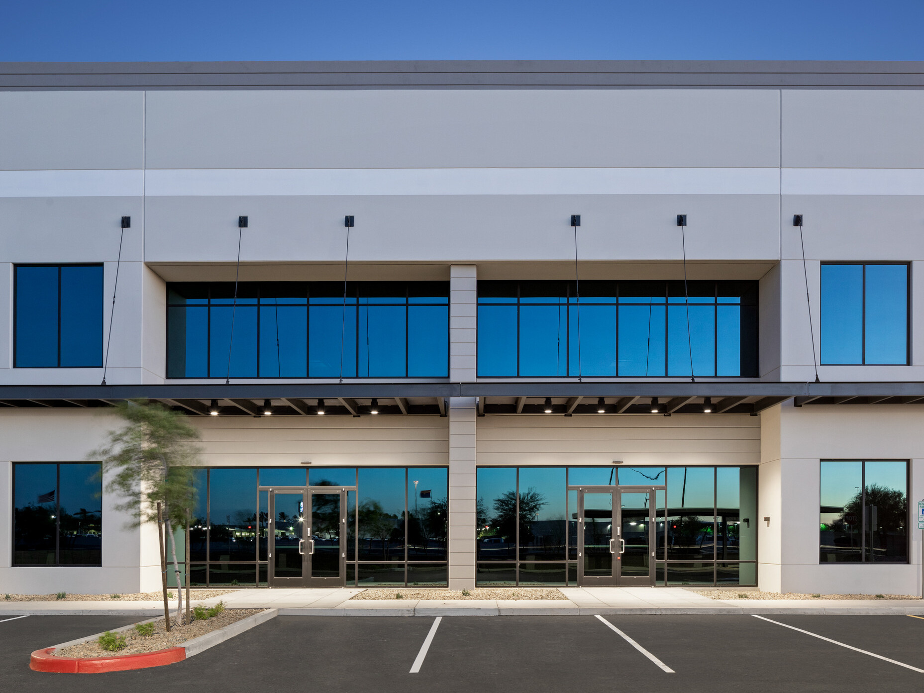 Avondale Commerce Park building entry; straight-on view of two tenant entrances side by side; slatted metal canopies entries; light to medium gray tilt-up facade with blue and white accent stripes