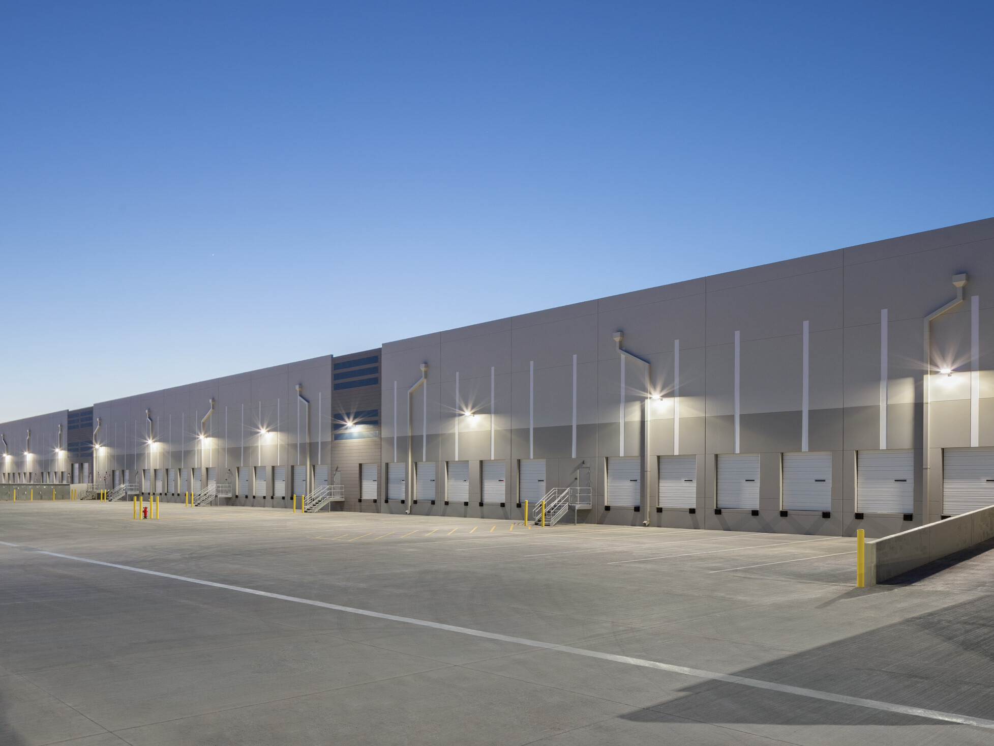 Avondale Commerce Park loading dock facade; repeated sequence of overhead dock doors spanning the length of the warehouse wall; clean industrial aesthetic in light to medium gray tilt-up panels