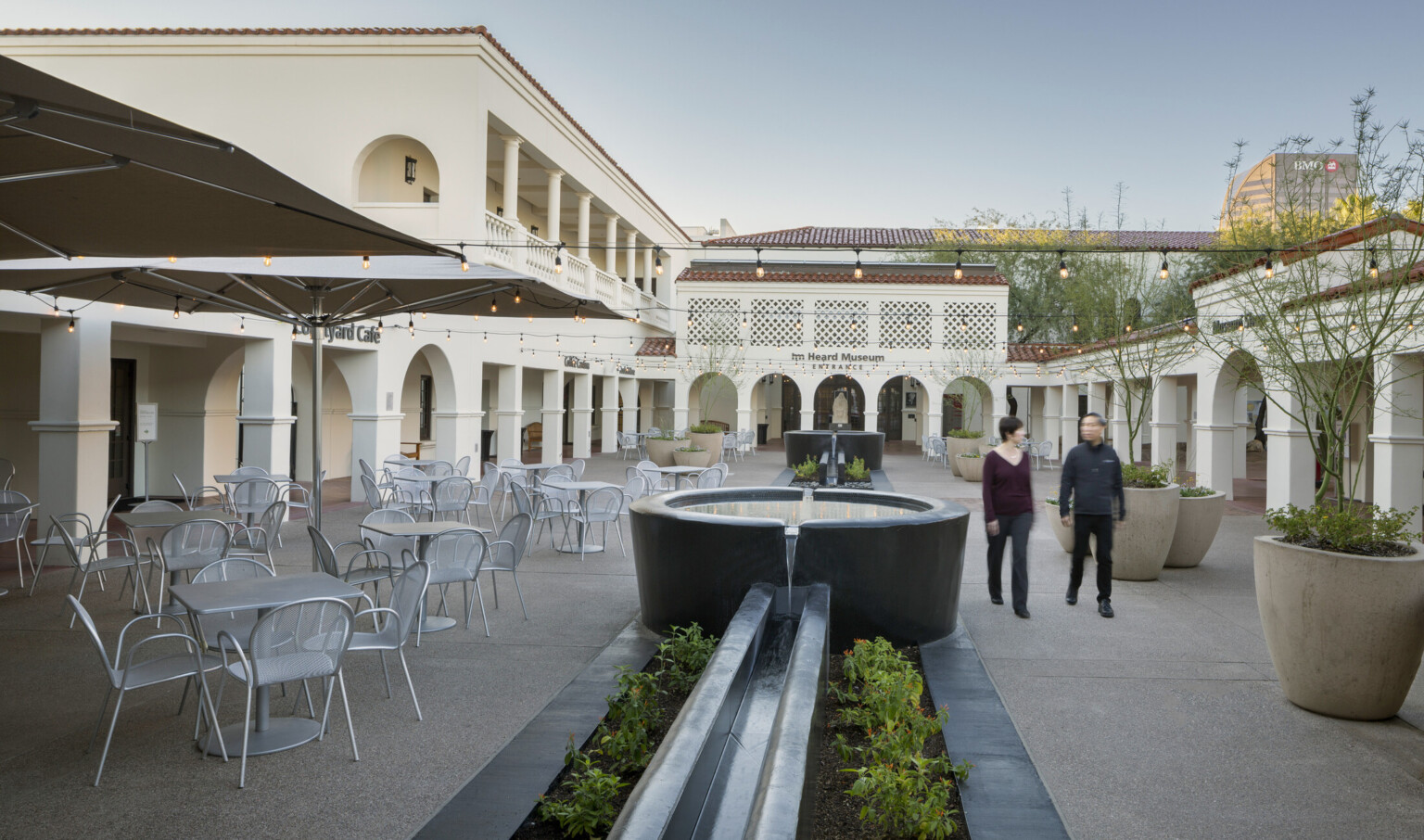 A courtyard with tables and chairs to the left; a fountain runs the central length and lights are strung across the width
