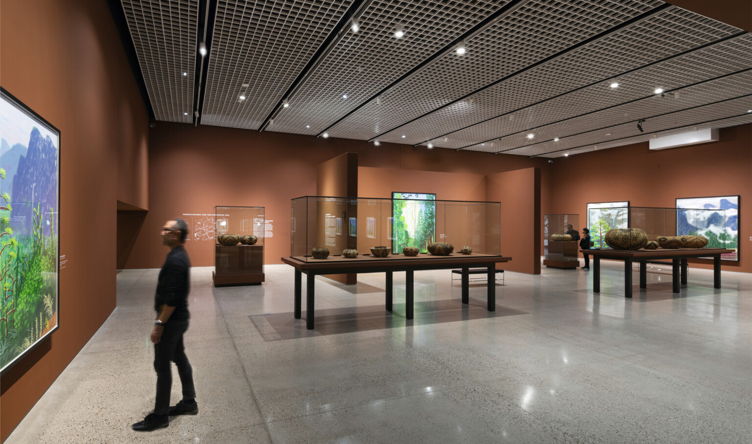 Orange brown gallery walls with vibrant green visual displays hanging on them. Native American pottery on display at center