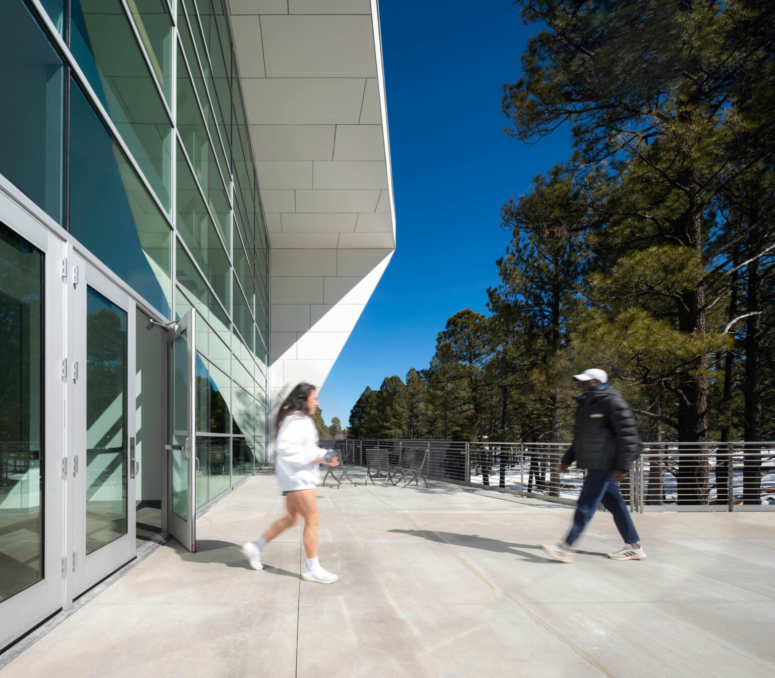 angular white paneled exterior canopy over glass facade with glass doors leading onto concrete plaza lined with wire railing