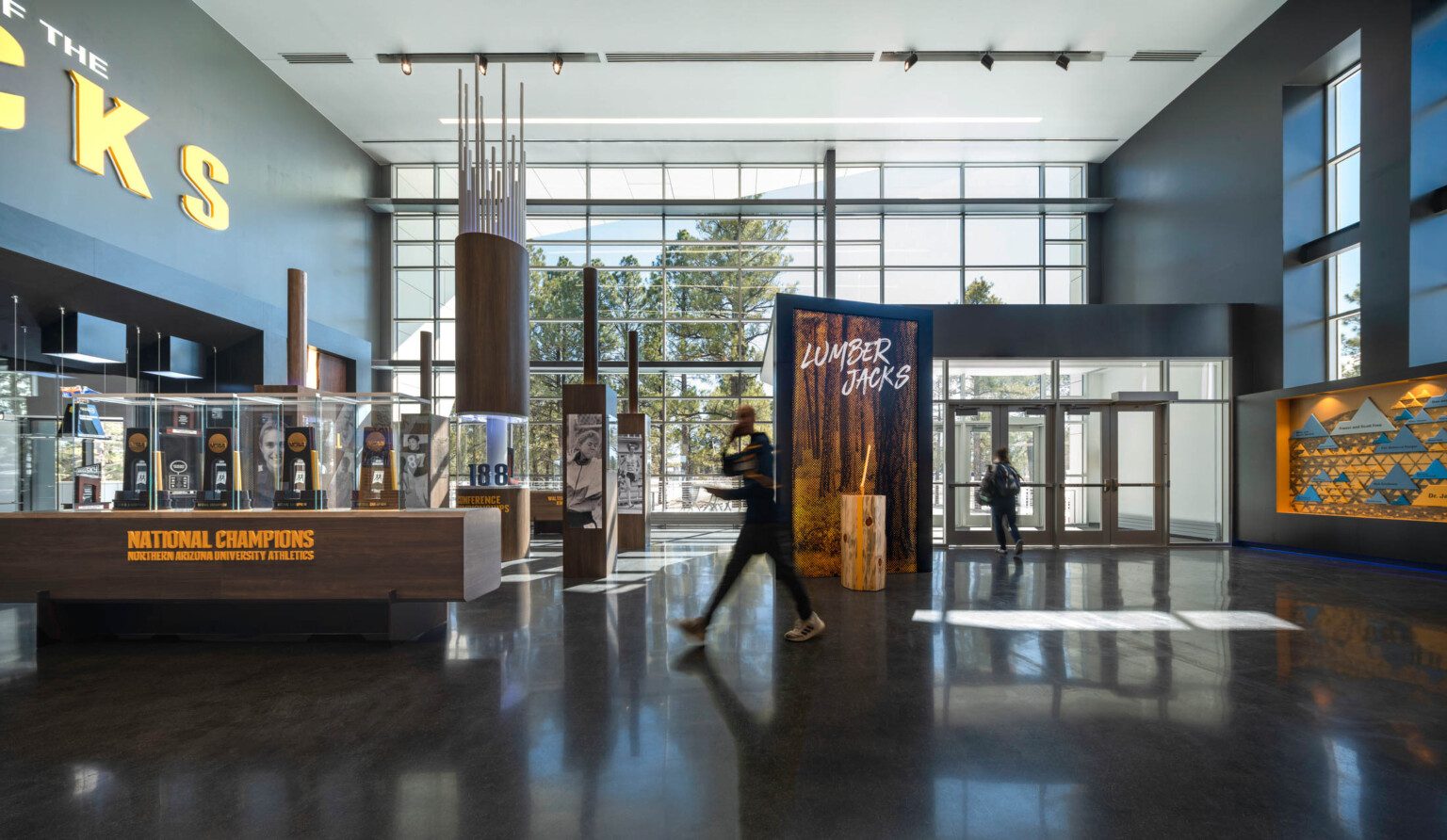 entry hall with glass and gray wall, trophy display on wood plinth. graphics in faux bois print and text spells lumber jacks