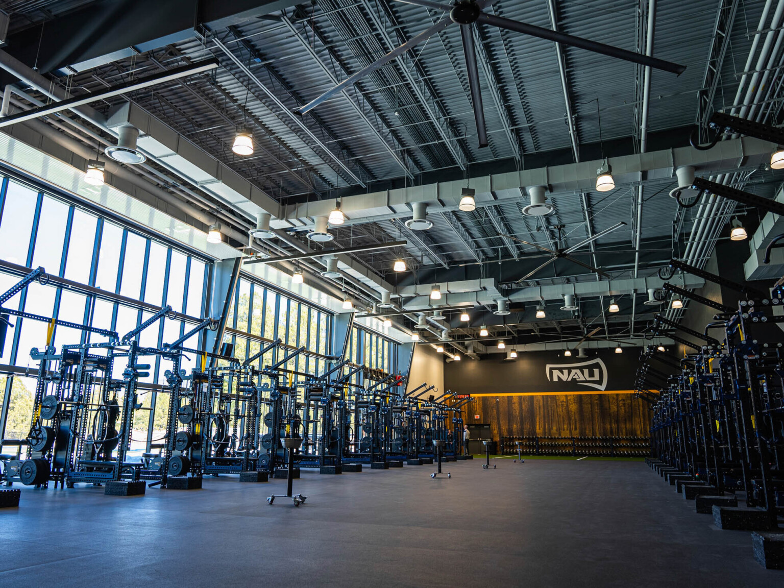high black open ceiling weight training room with floor to ceiling operable glass doors and super graphic wall with NAU logo