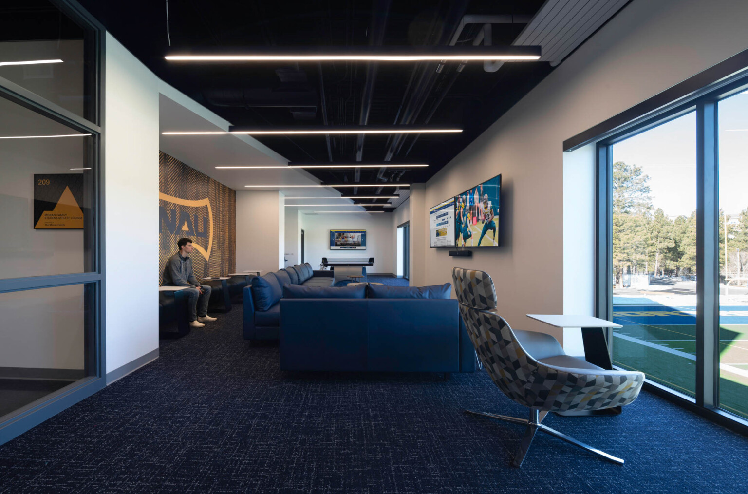 blue carpet, white and glass walls, a black ceiling and pendant lights with geometric upholstered chair and blue leather sofas