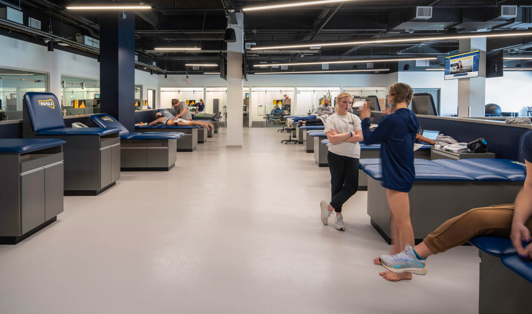 open room with columns, white floors and open ceilings painted plan with long pendant lights and blue upholstered exam tables