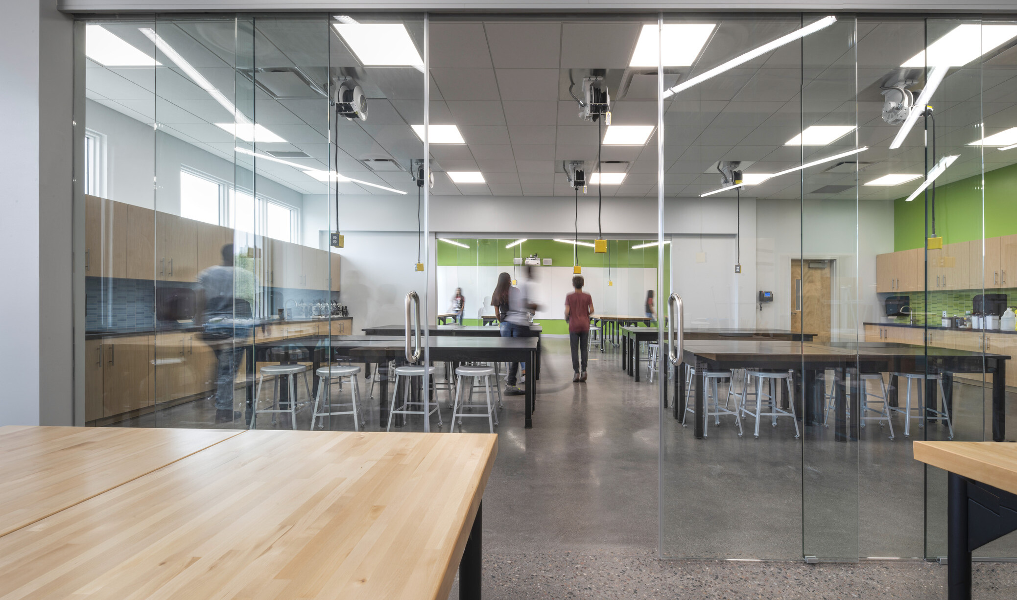 workshop in a middle school with wood tables in the front area, glass retractable walls separate the classrooms