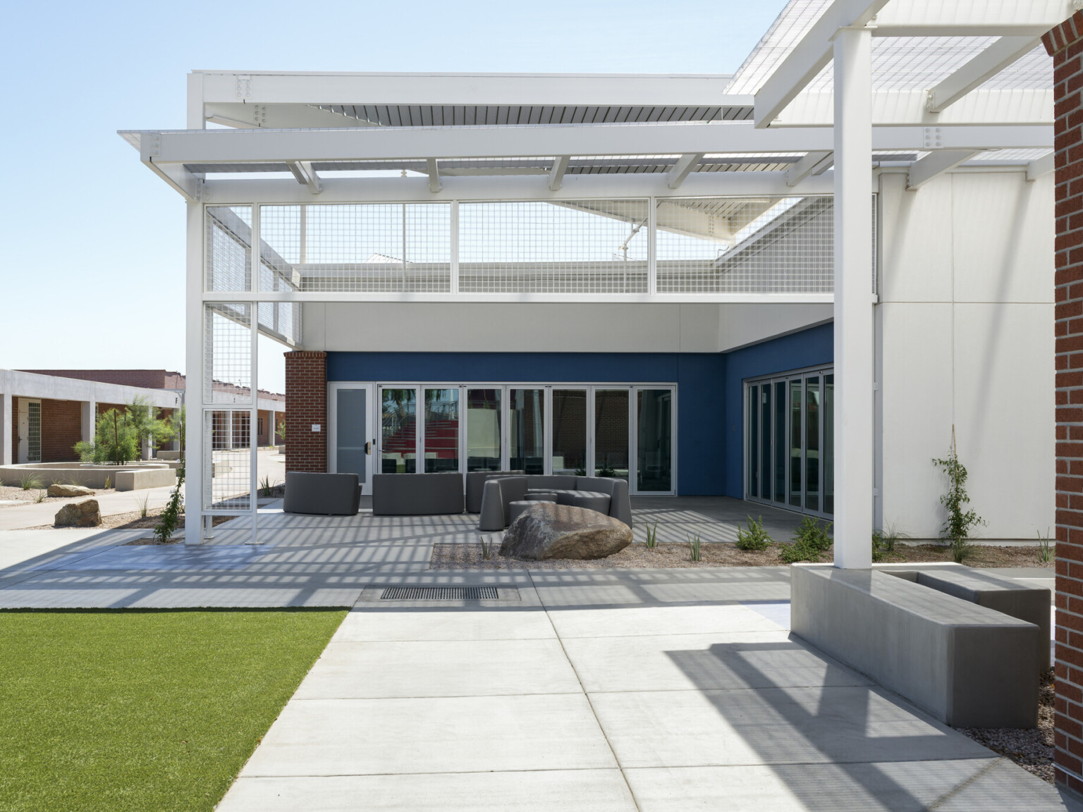 exterior of the quad, white building with white angular steel roof, concrete pathways and concrete outdoor seating, grass, landscaping