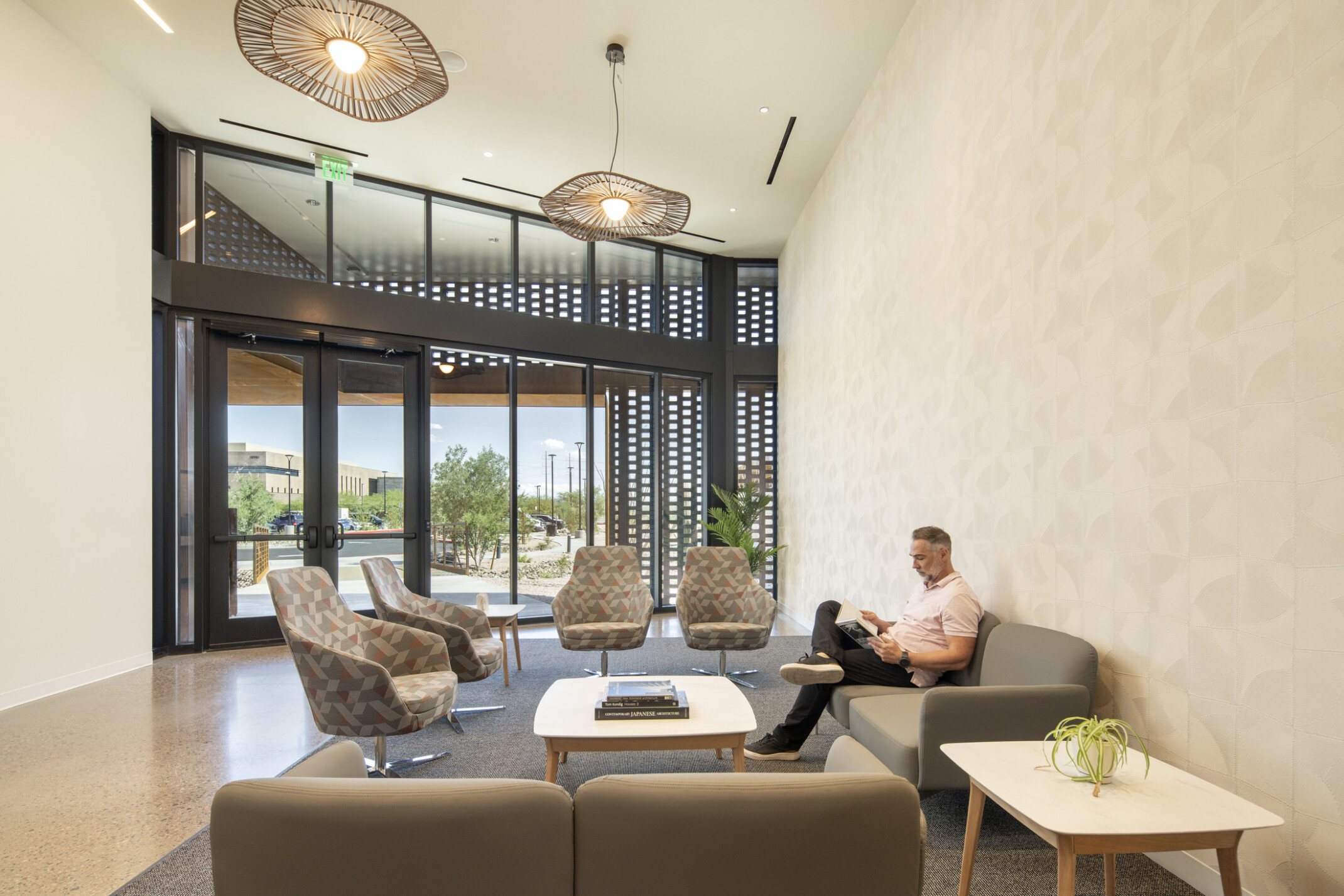 Modern healthcare waiting area with lounge seating, natural daylight, decorative lighting, and a person seated on a sofa reading.