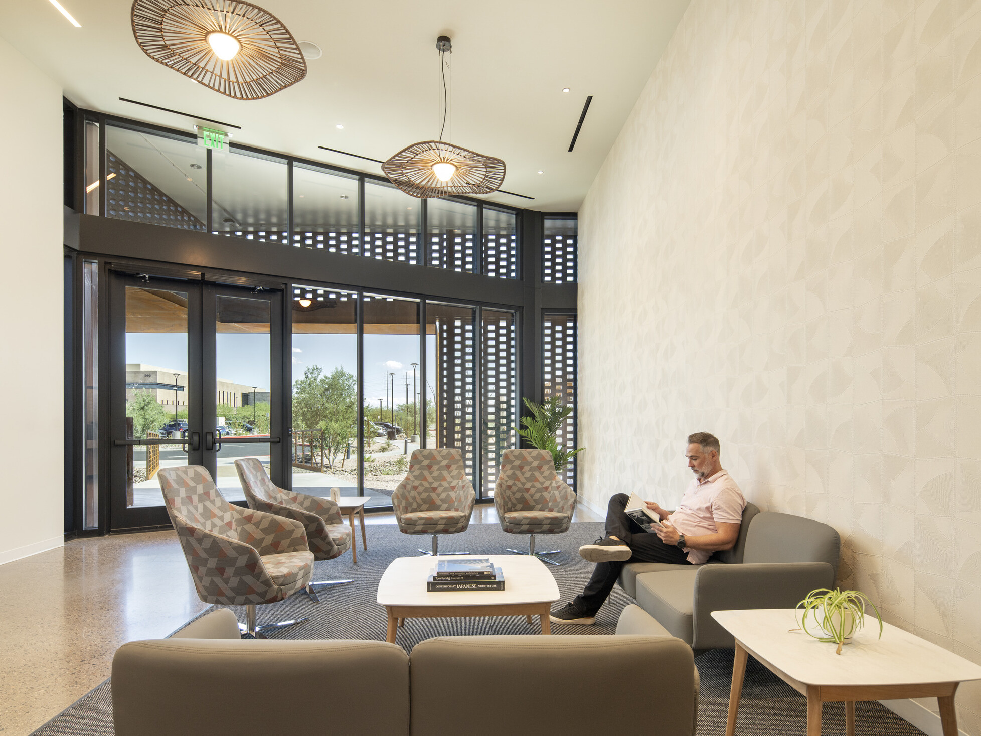 Modern healthcare waiting area with lounge seating, natural daylight, decorative lighting, and a person seated on a sofa reading.