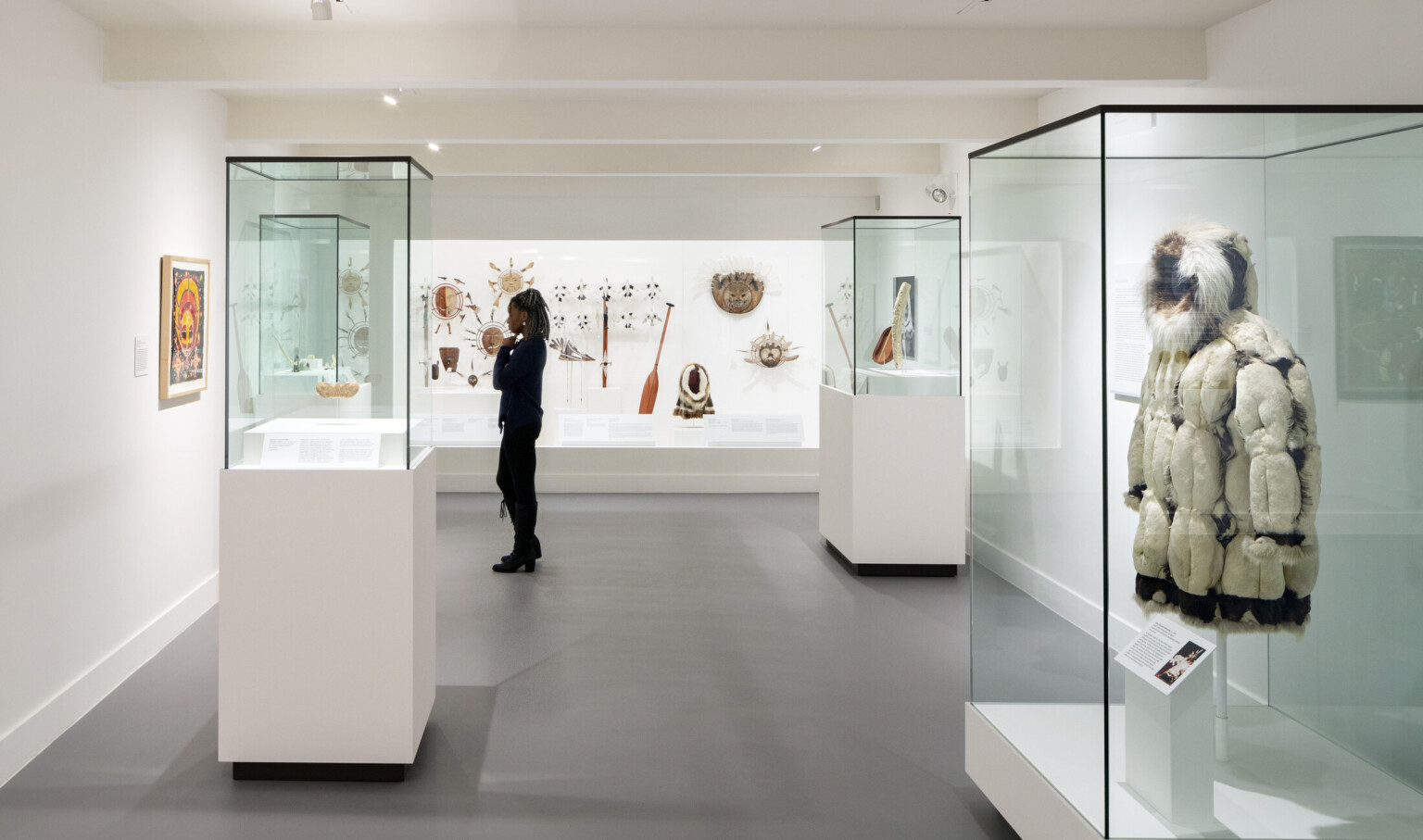 A gallery with paintings and a display of dressed mannequins, under a wood ceiling with exposed black support beams and pipes