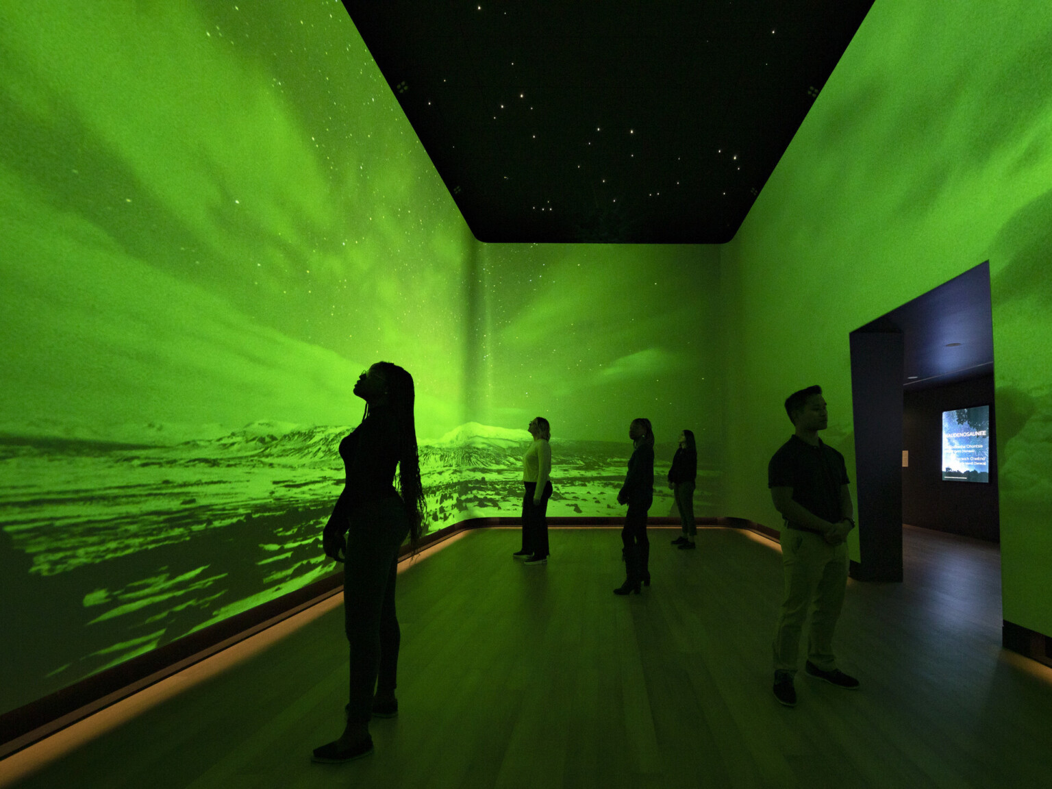 An immersive art exhibit at the Heard Museum with screens on all visible walls of the room showing the Northern Lights among snow-capped hills colorized with bright green An immersive art exhibit at the Heard Museum with screens on all visible walls of the room showing the Northern Lights among snow-capped hills colorized with bright green