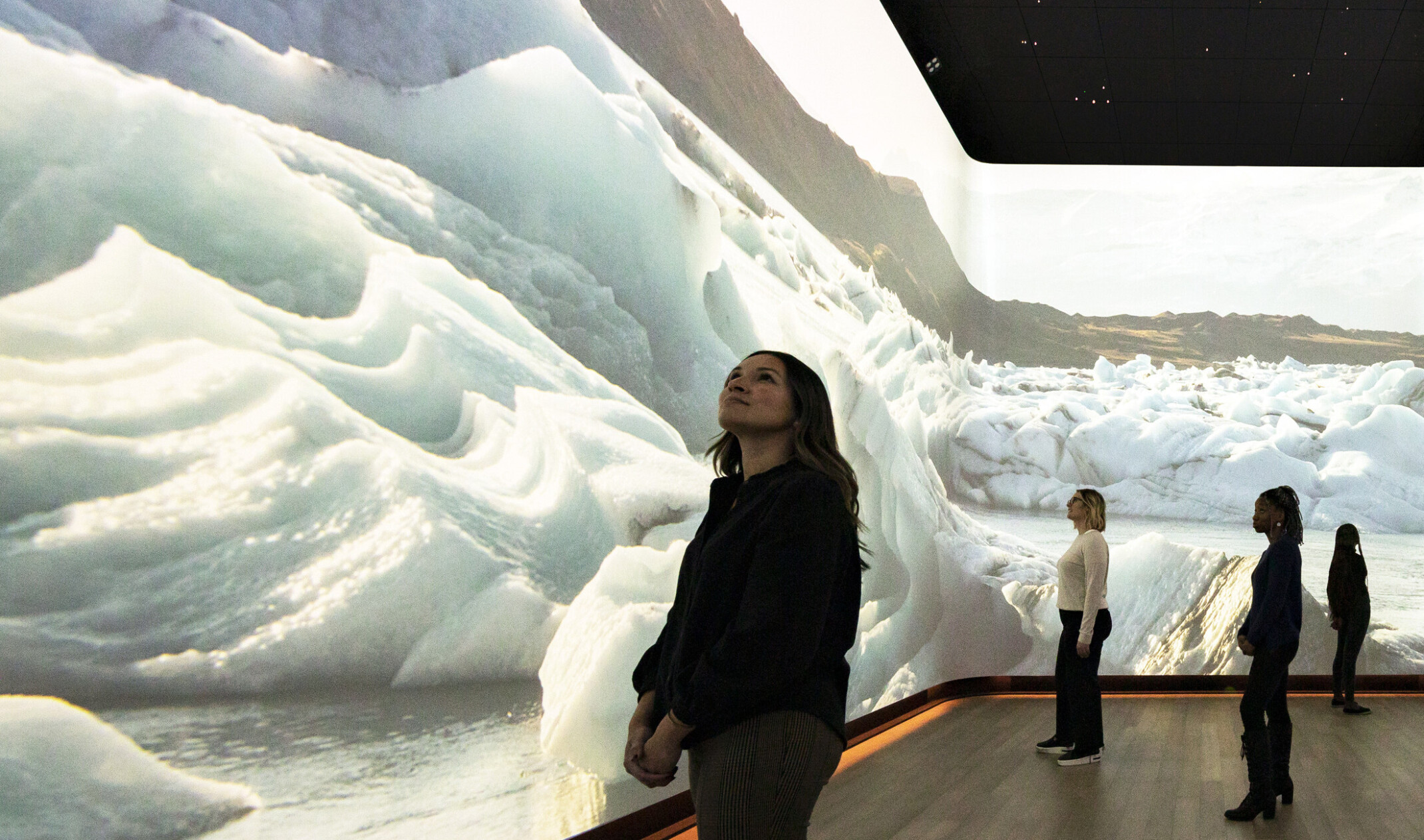 Woman stands in front of immersive 360 degree video art display of snow dunes and ice, interactive museum