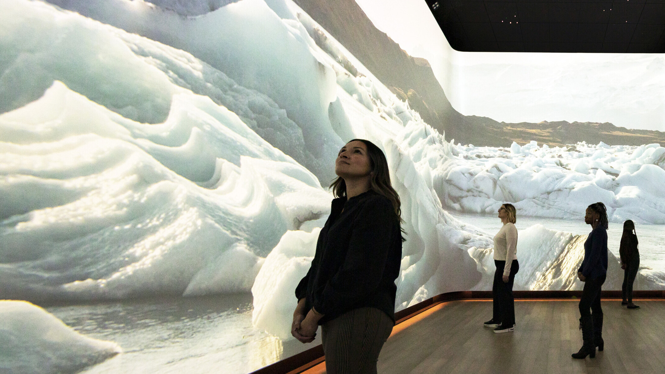 Woman stands in front of immersive 360 degree video art display of snow dunes and ice, interactive museum