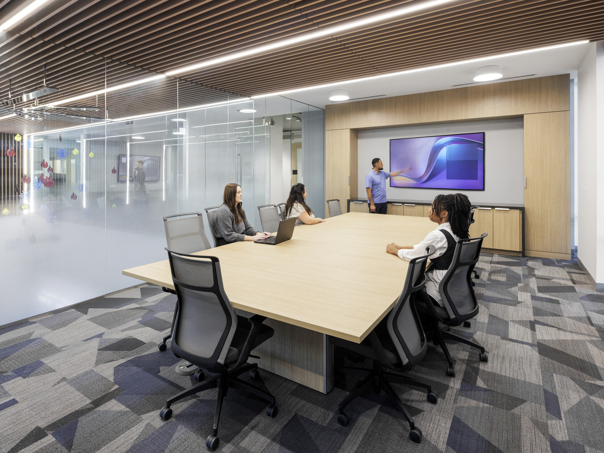 ub-Zero Group conference room; wood slat ceiling with integrated lighting extending from reception lobby aesthetic; large meeting table seating 10-12; full-wall credenza in light wood